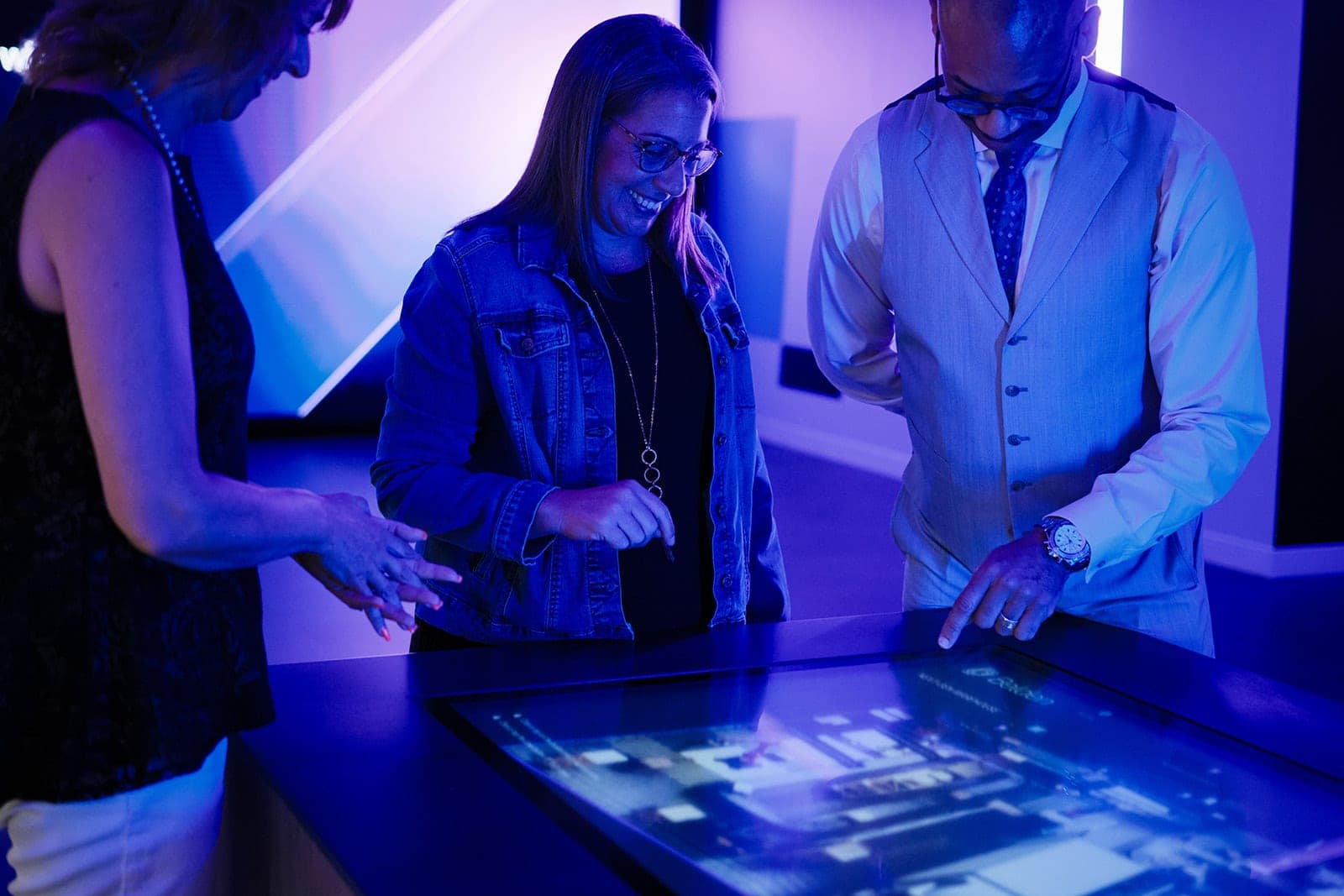 Two colleagues leaning over the Belden interactive touch table together, a candid working moment photographed in low light in St. Louis
