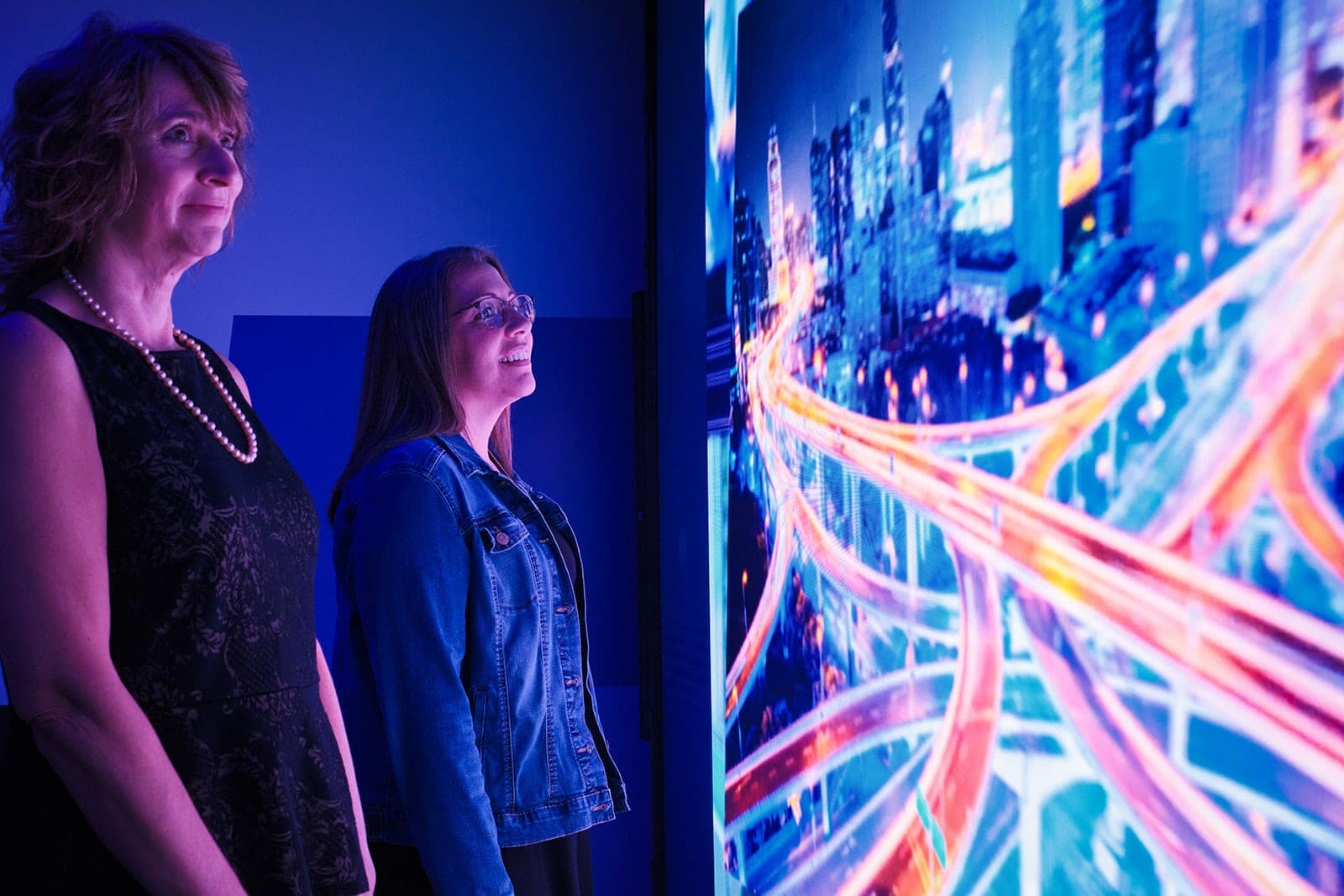 Two people in profile lit only by the Belden video wall as it fills with a night cityscape, candid corporate photography in St. Louis