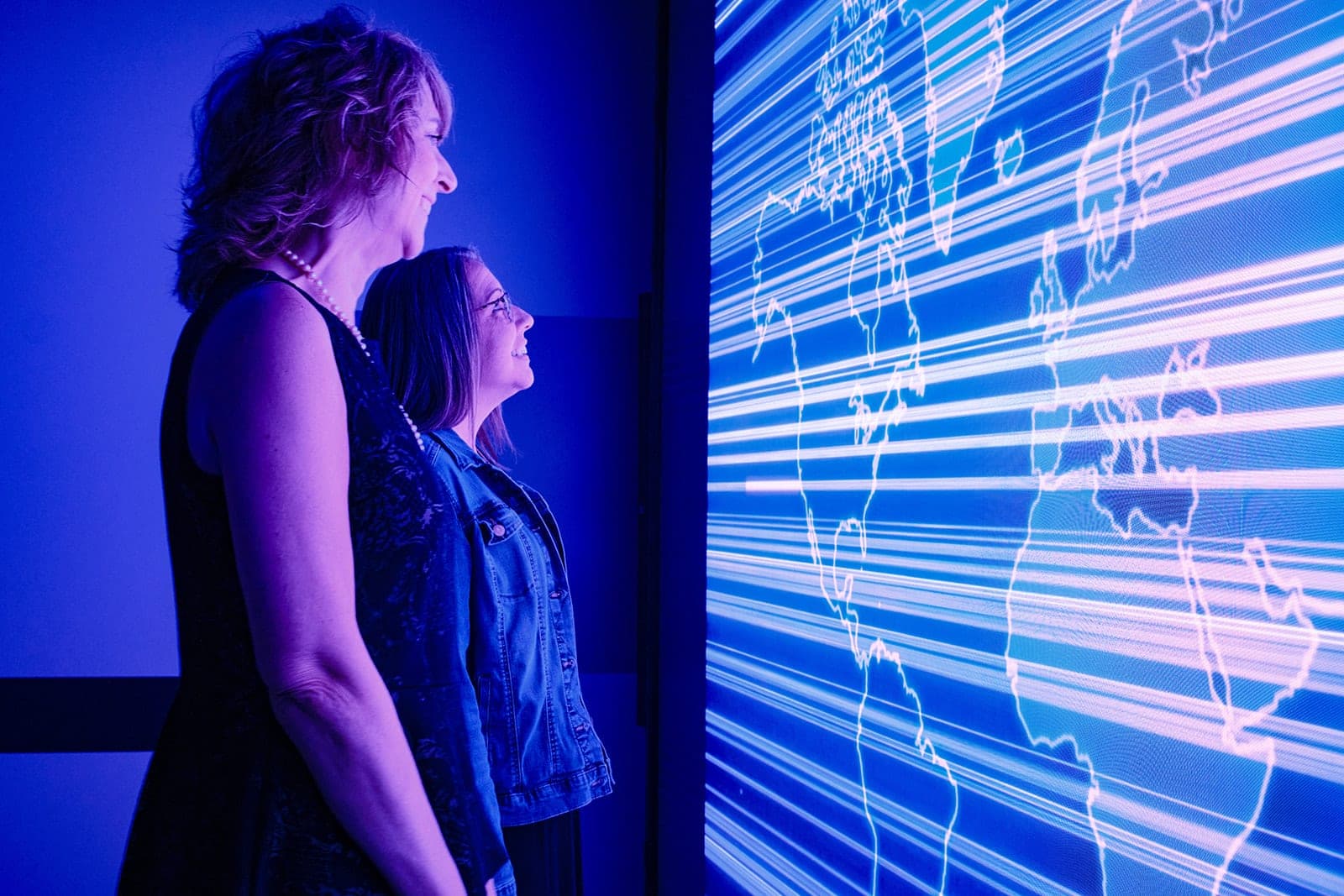 Two colleagues watching the Belden LED video wall as it runs a world map traced with light, corporate lifestyle photography in a St. Louis experience center