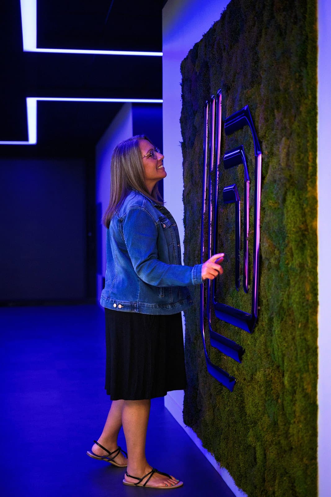 Someone reaching up to touch the illuminated Belden mark on the preserved moss wall, corporate lifestyle photography in St. Louis