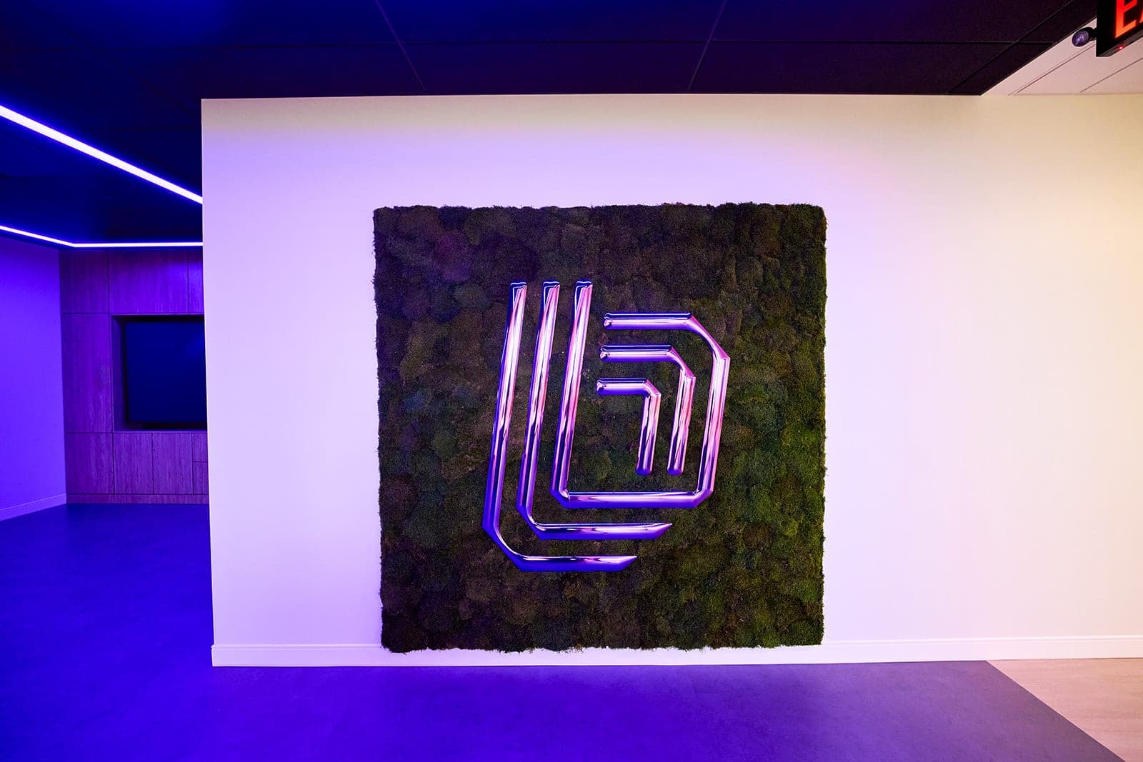 The illuminated chrome Belden mark mounted on the preserved moss wall, detail photography of a brand installation in a St. Louis office