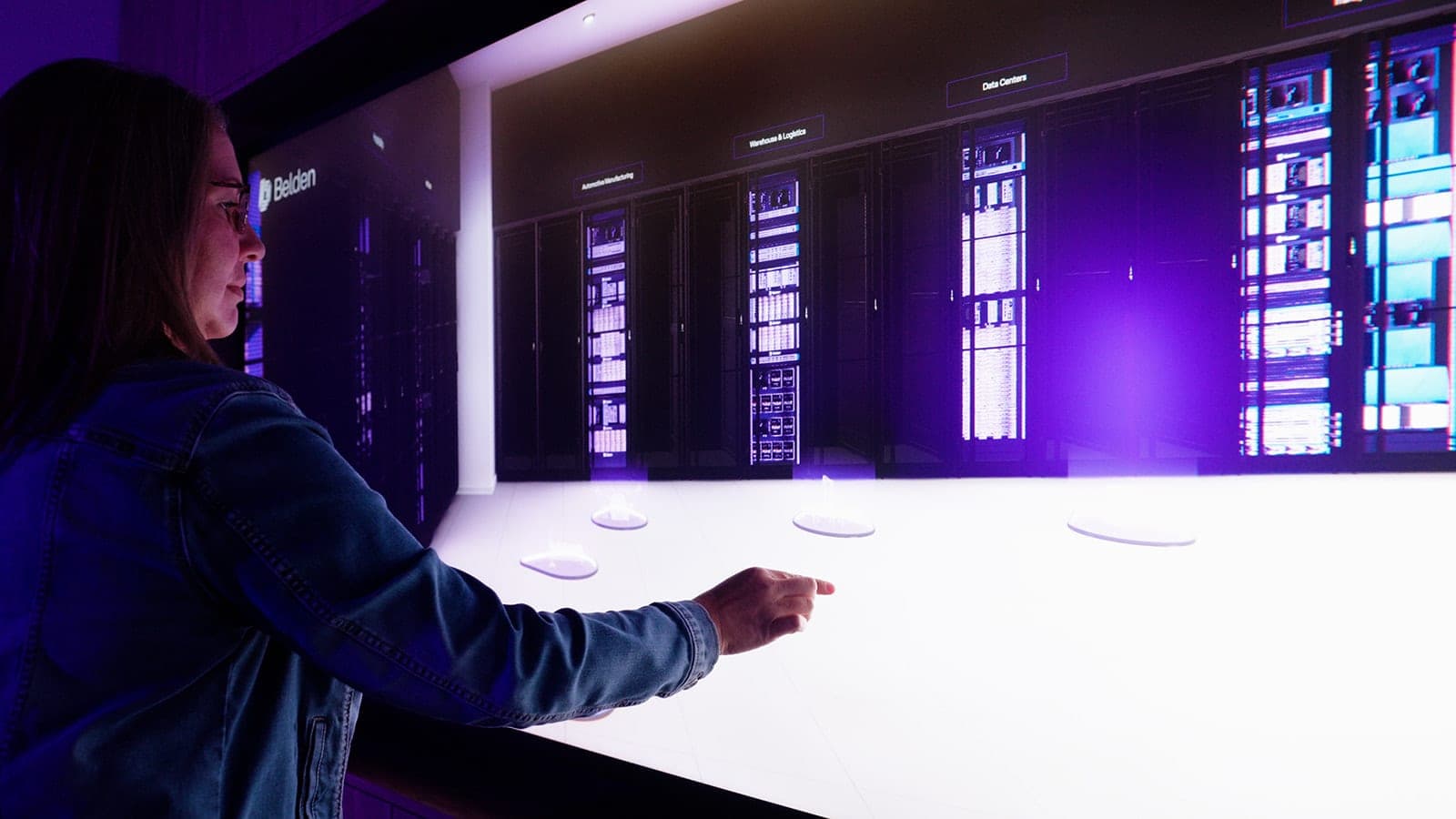 A frame from the Belden brand film: a hand moving across the touch table as it shows illuminated server rack graphics, cinematic detail from a one-day corporate production in St. Louis
