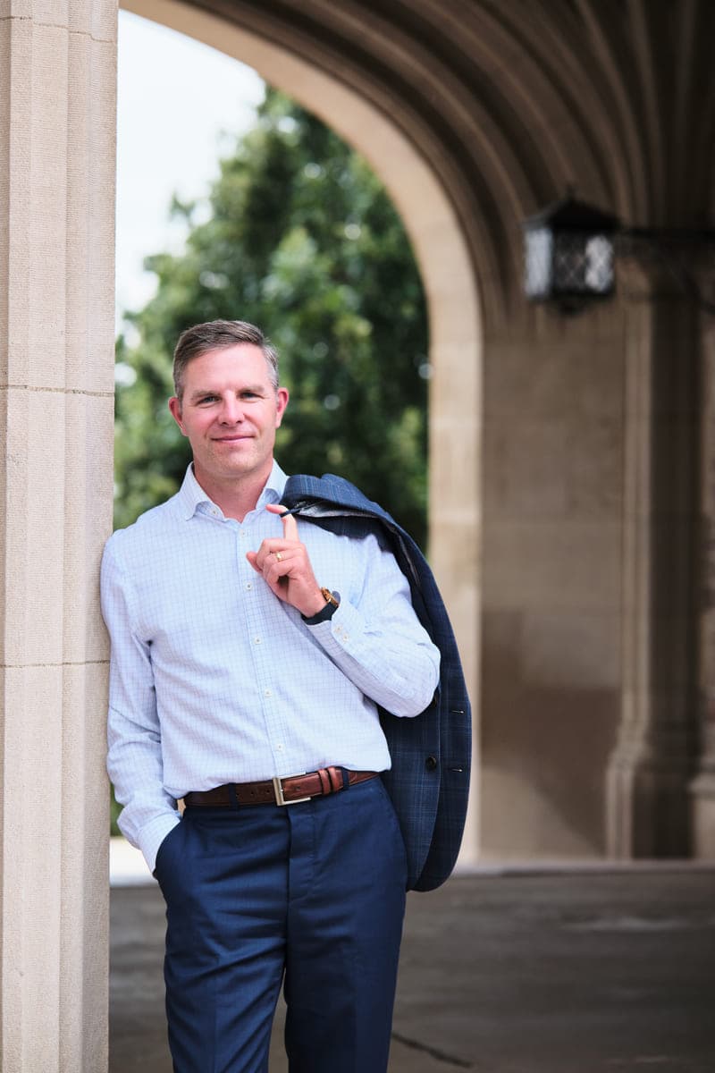 Drew Forrester leaning against a stone column with a blazer over his shoulder, outdoor executive portrait