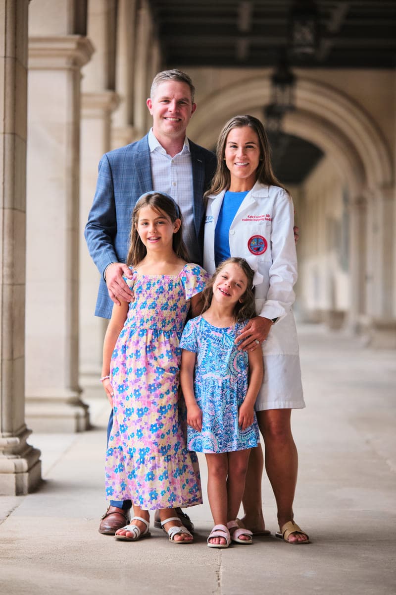 Drew Forrester with his wife in her physician's white coat and their two daughters under a stone colonnade, family portrait for a financial firm website