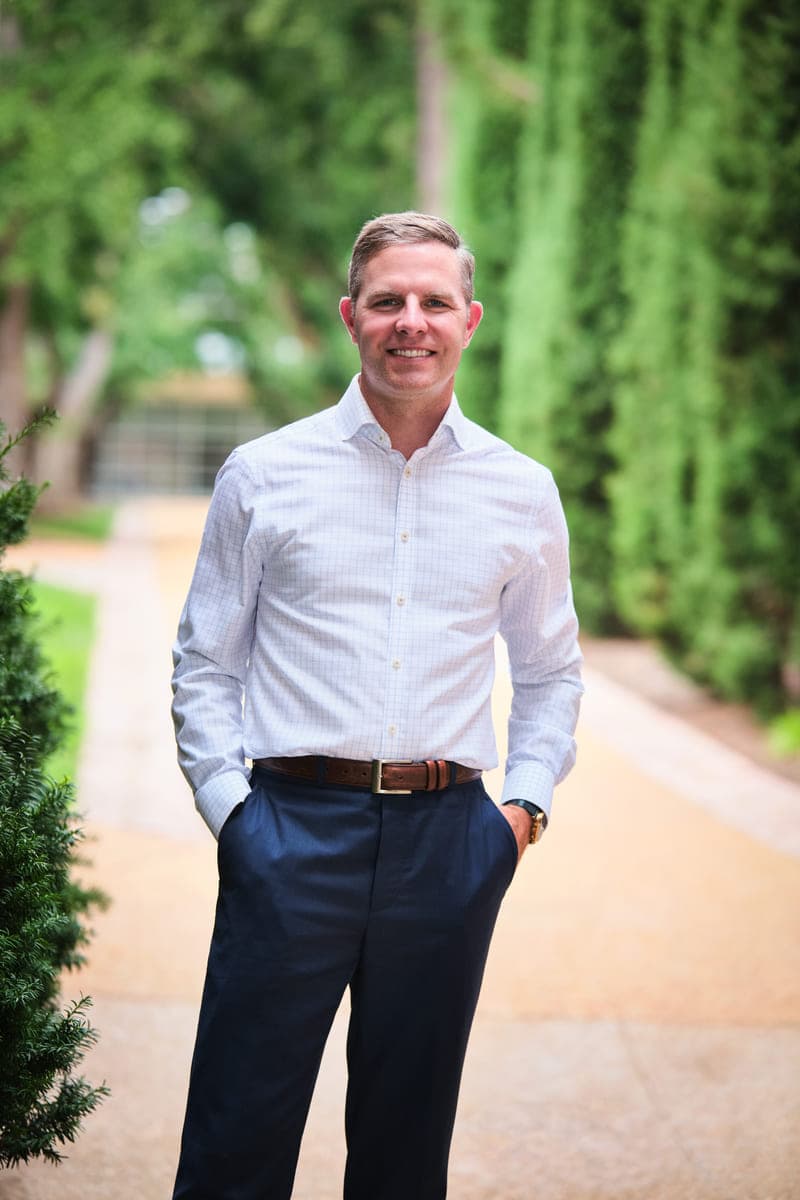 Drew Forrester standing on a garden walkway in a light checked shirt and navy trousers, outdoor branding portrait in St. Louis