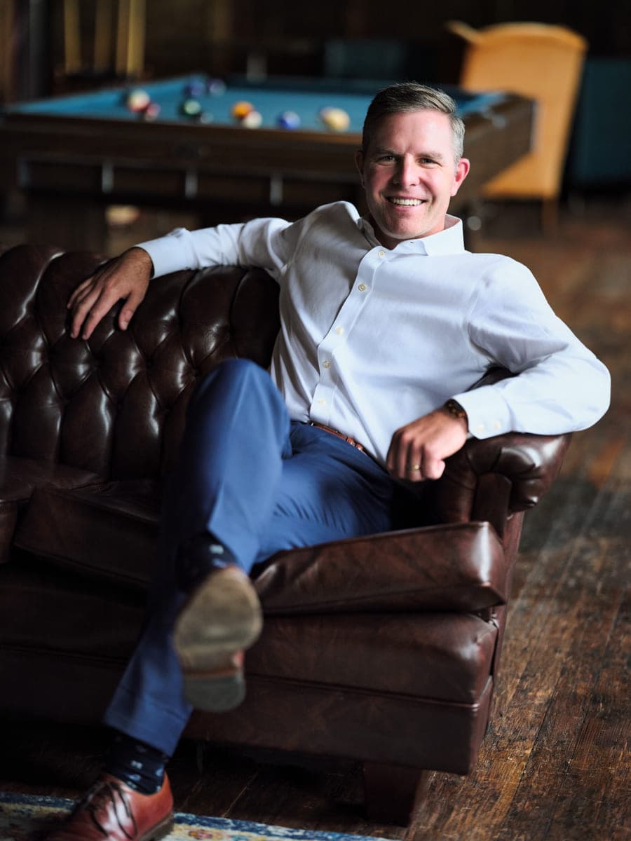 Drew Forrester in a white dress shirt reclining on a leather sofa, casual personal branding portrait