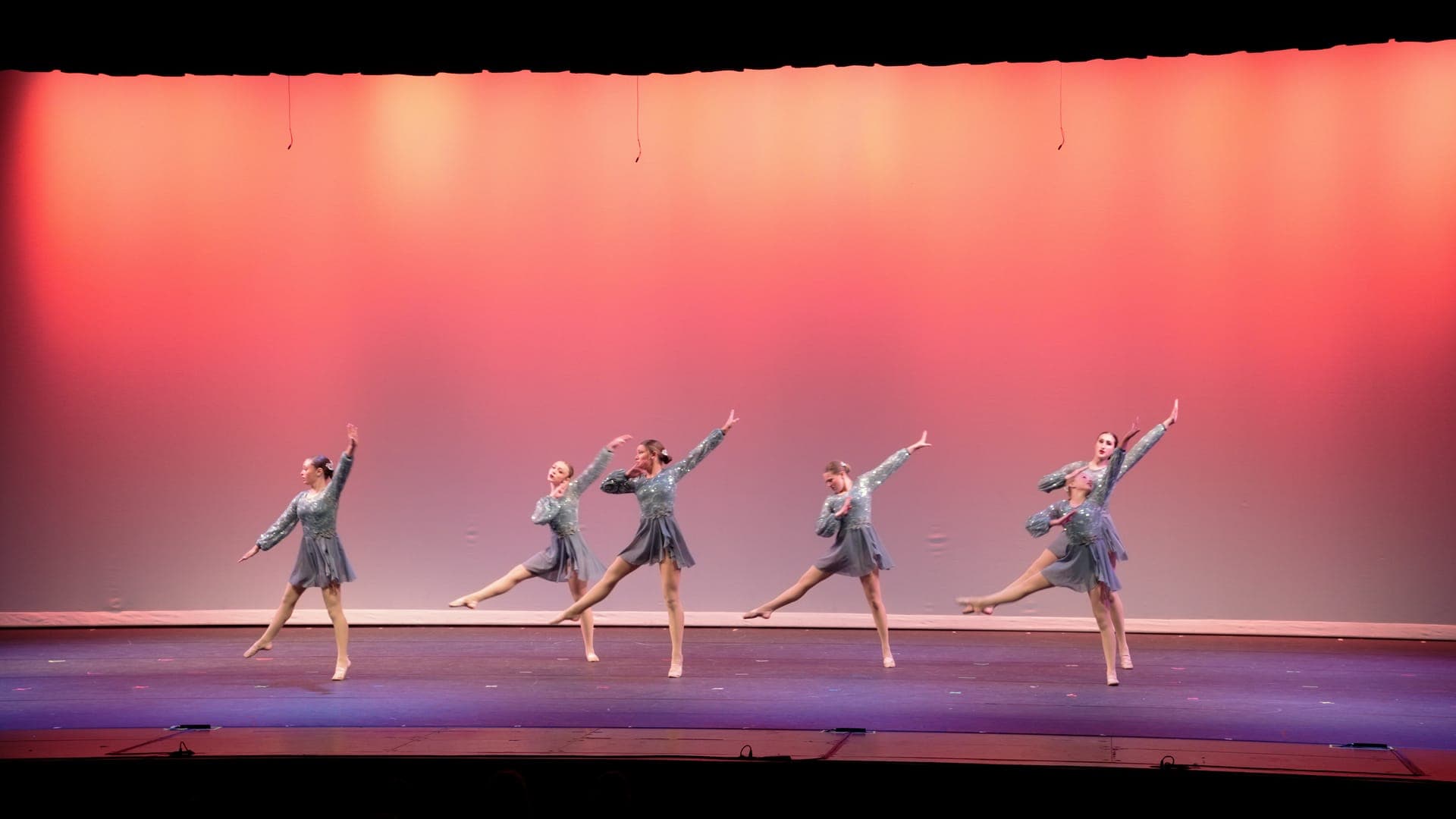 Four dancers in gray hold a synchronized arabesque during a St. Louis dance recital