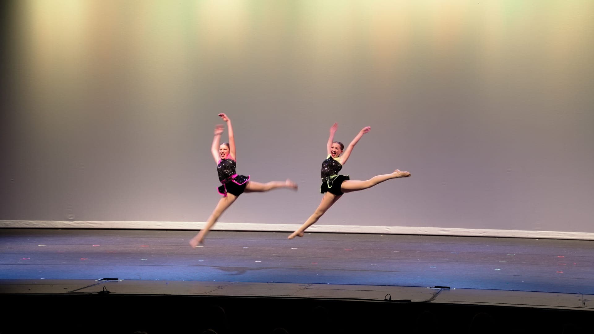 Two dancers in matching mid-air split leaps on a St. Louis dance recital stage
