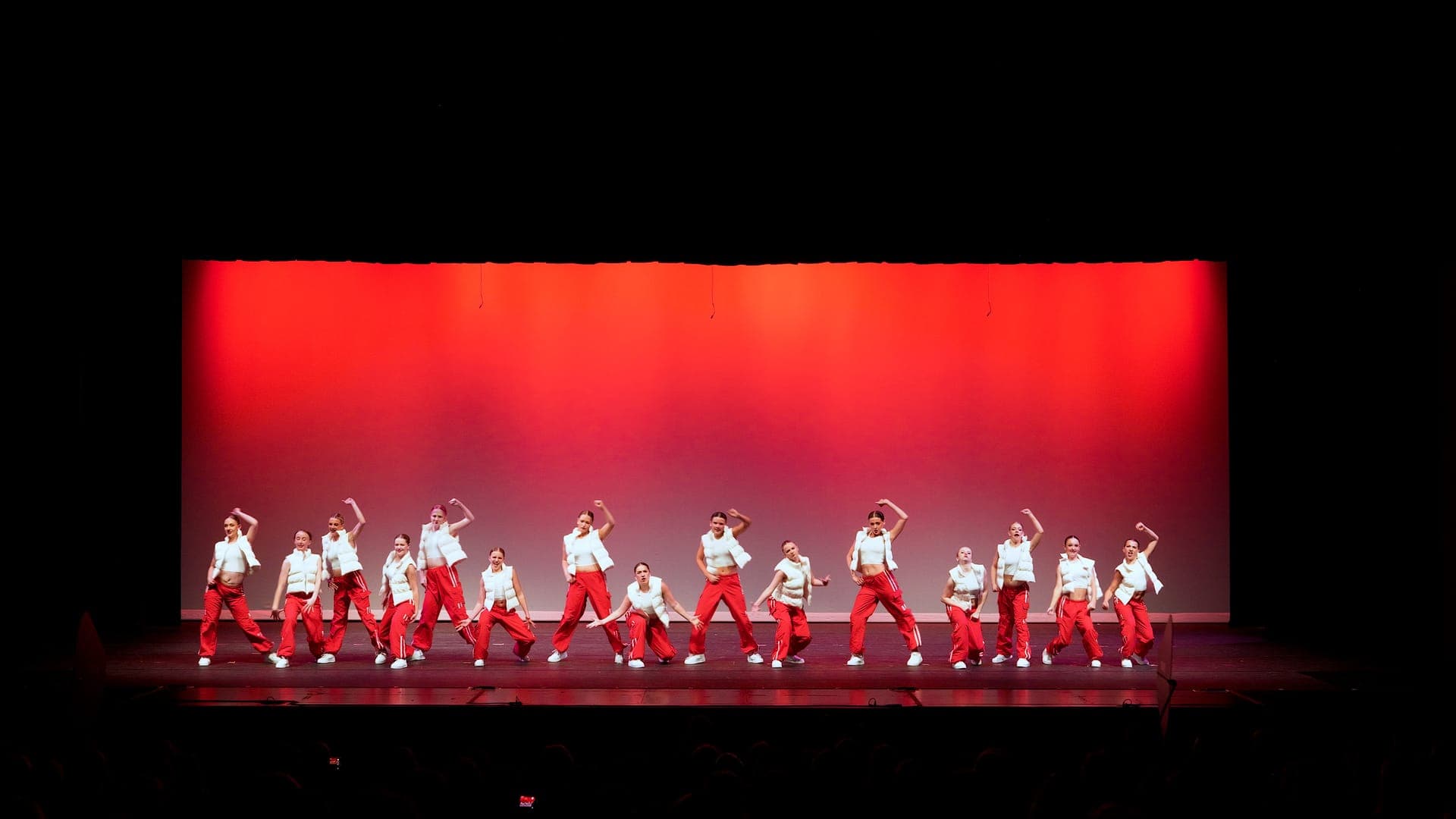 Hip hop dance team in red holding a synchronized pose under red light at a St. Louis dance recital