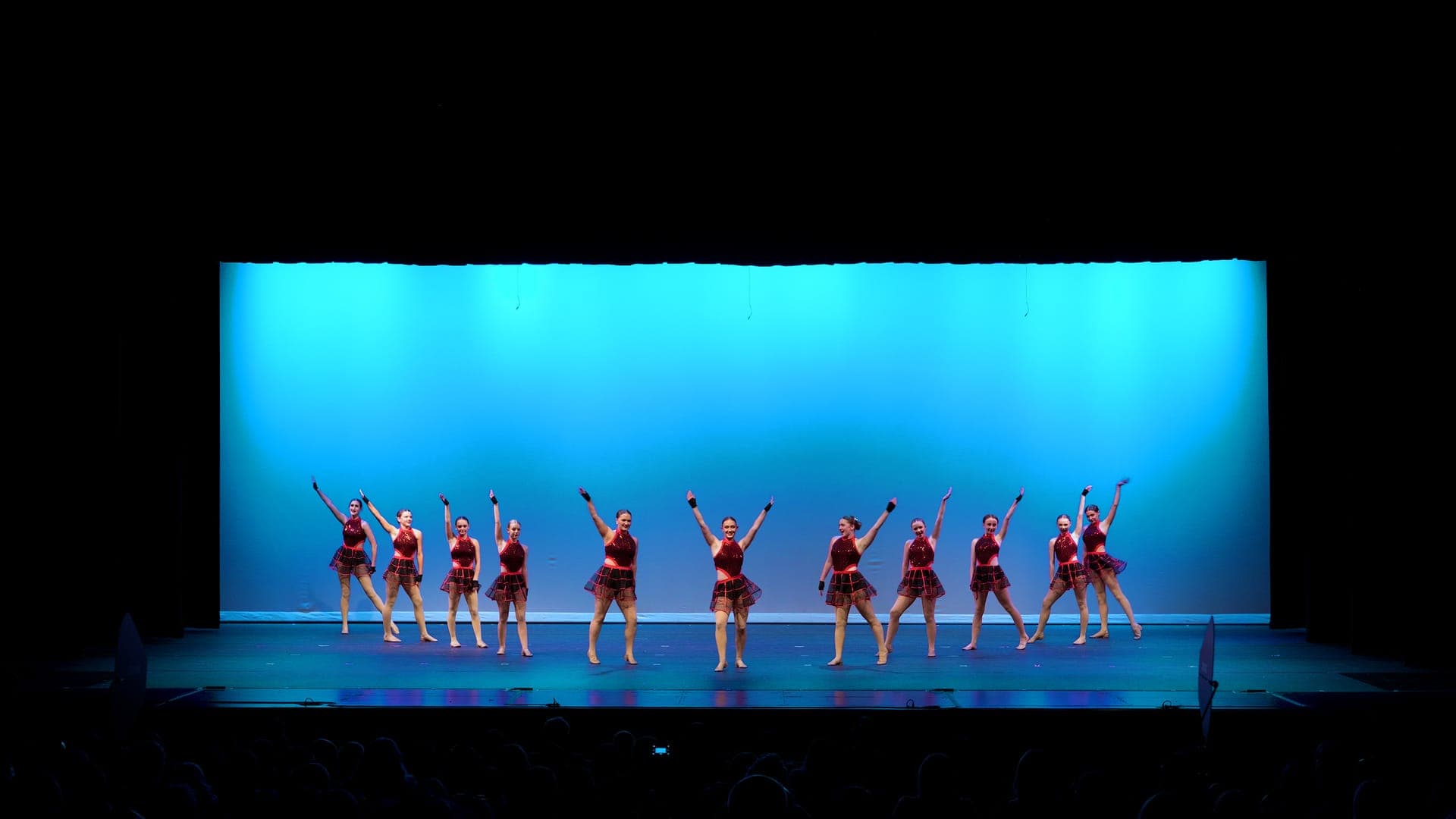 Kick line of dancers in red plaid with legs extended at a St. Louis dance recital