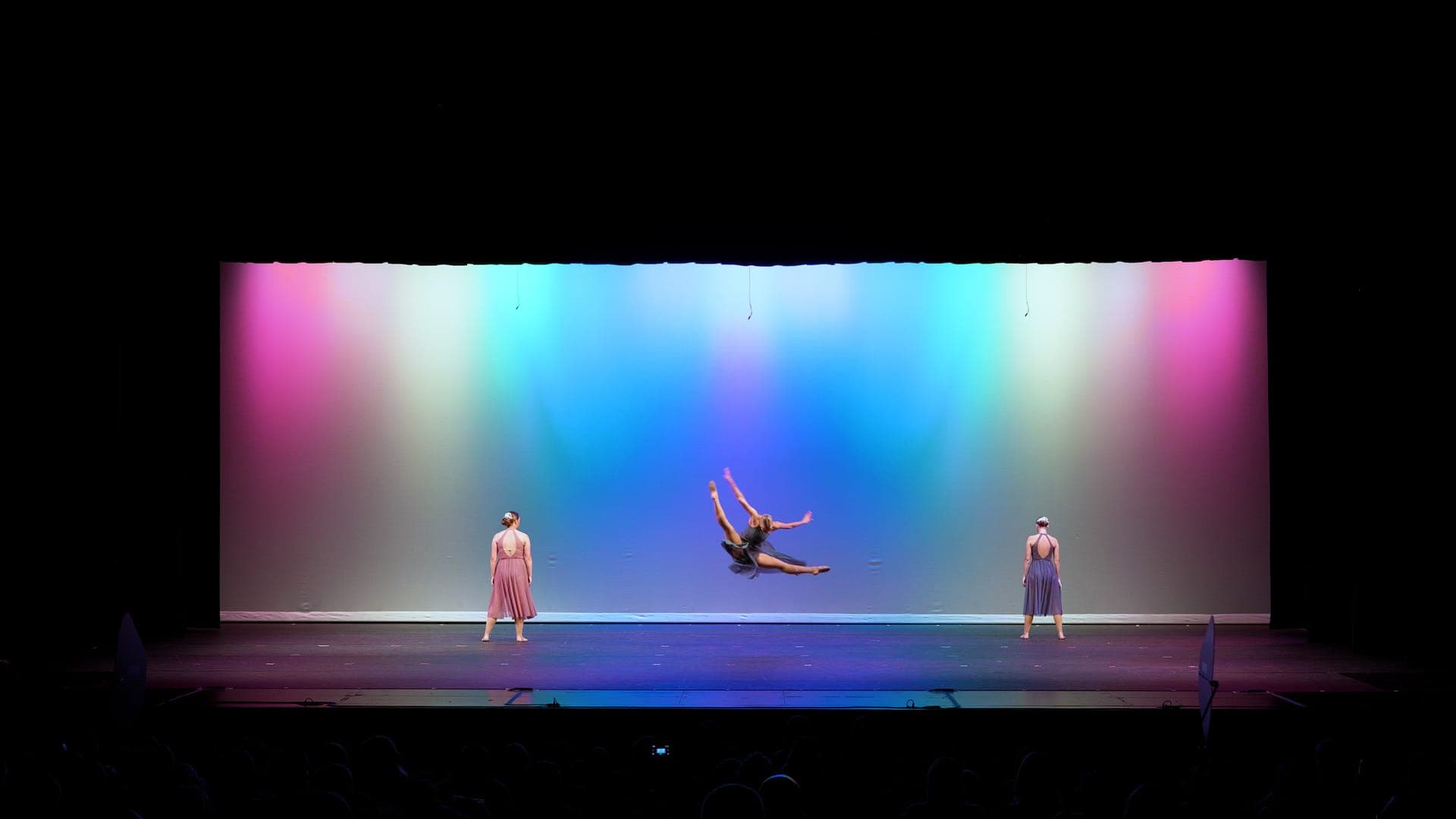A dancer leaps in a mid-air split between two dancers at a St. Louis dance recital