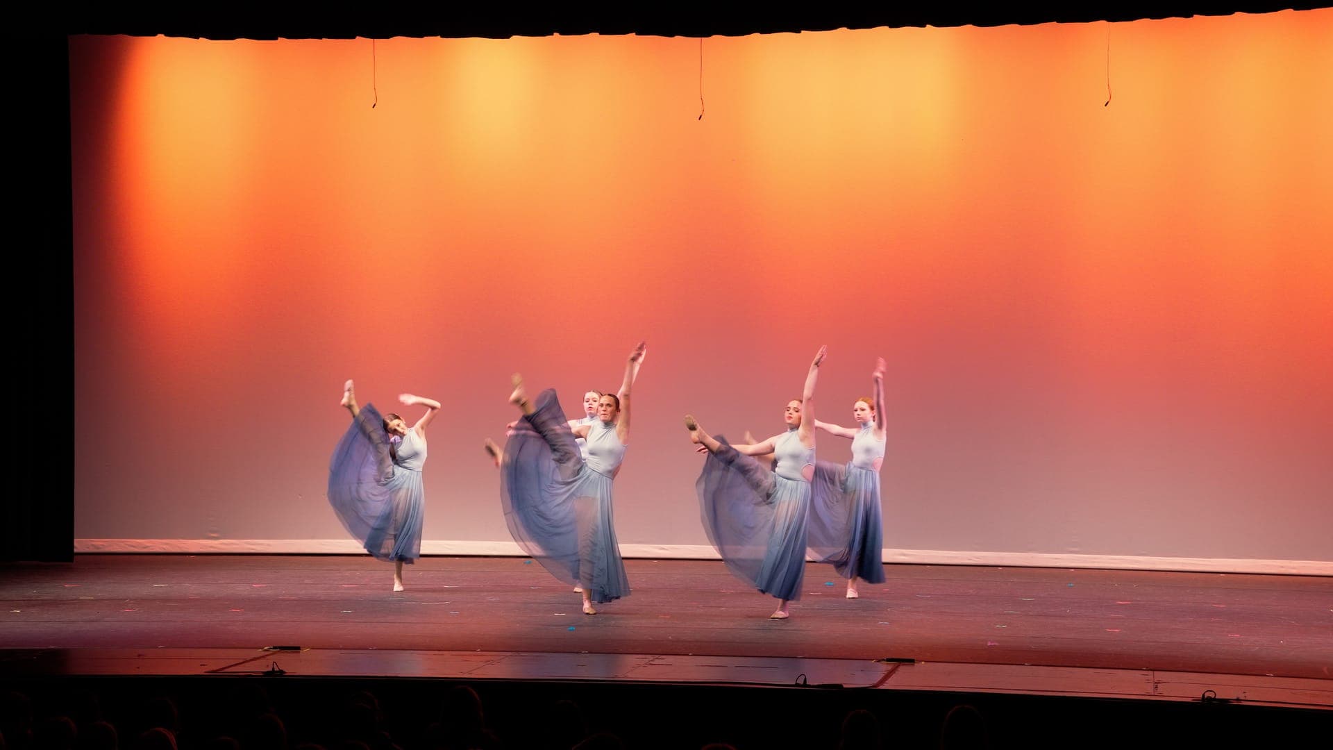 Dancers extend one leg in unison with flowing blue skirts at a St. Louis dance recital