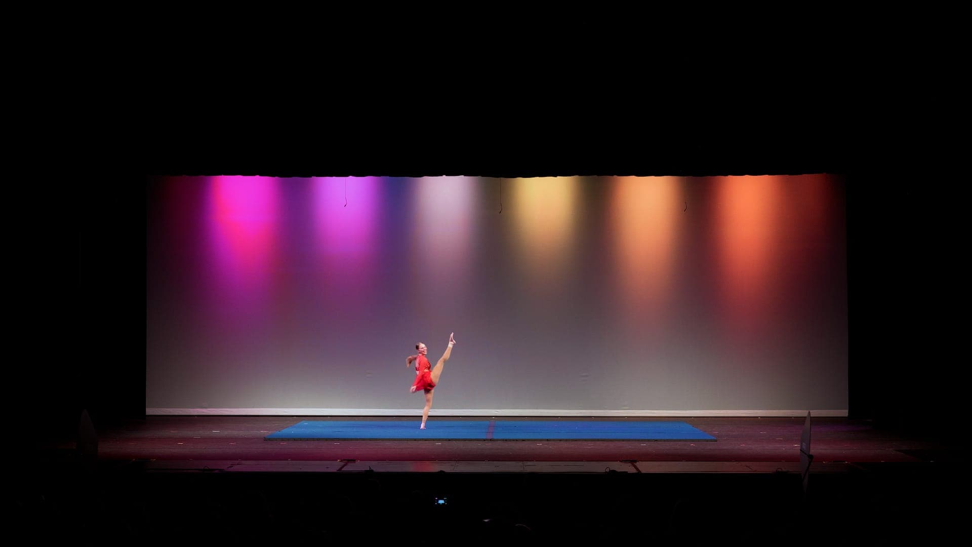Solo dancer in red holding a full vertical leg extension at a St. Louis dance recital