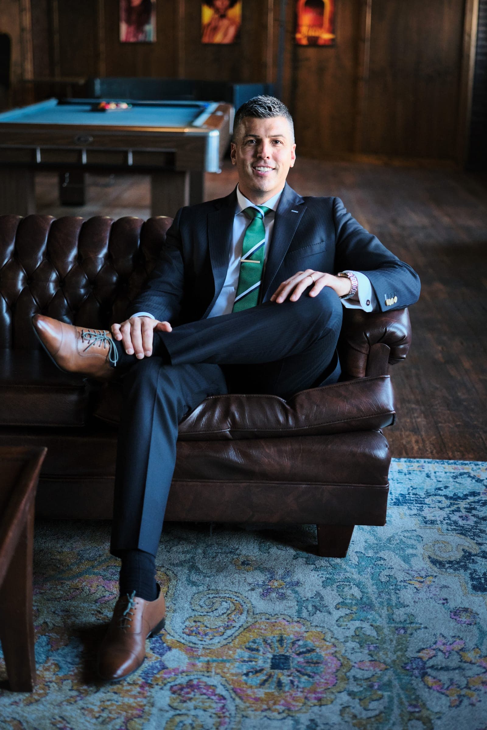 Attorney at The Dixon Injury Firm seated in a brown leather chesterfield in a wood-panelled room with a pool table, environmental portrait in St. Louis by Henry David Photography