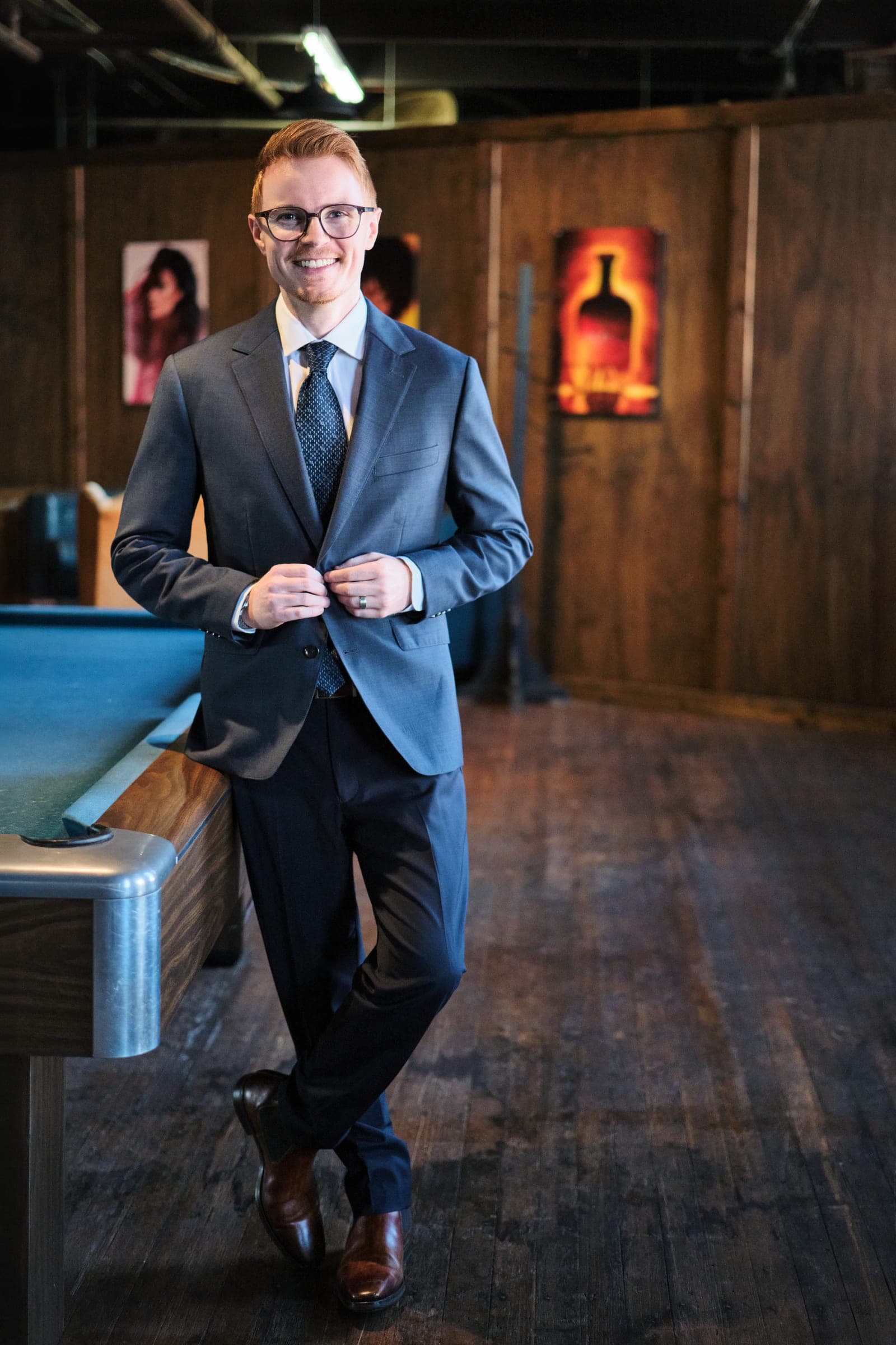 Attorney at The Dixon Injury Firm buttoning his suit jacket beside a pool table in a wood-panelled room, environmental portrait in St. Louis by Henry David Photography