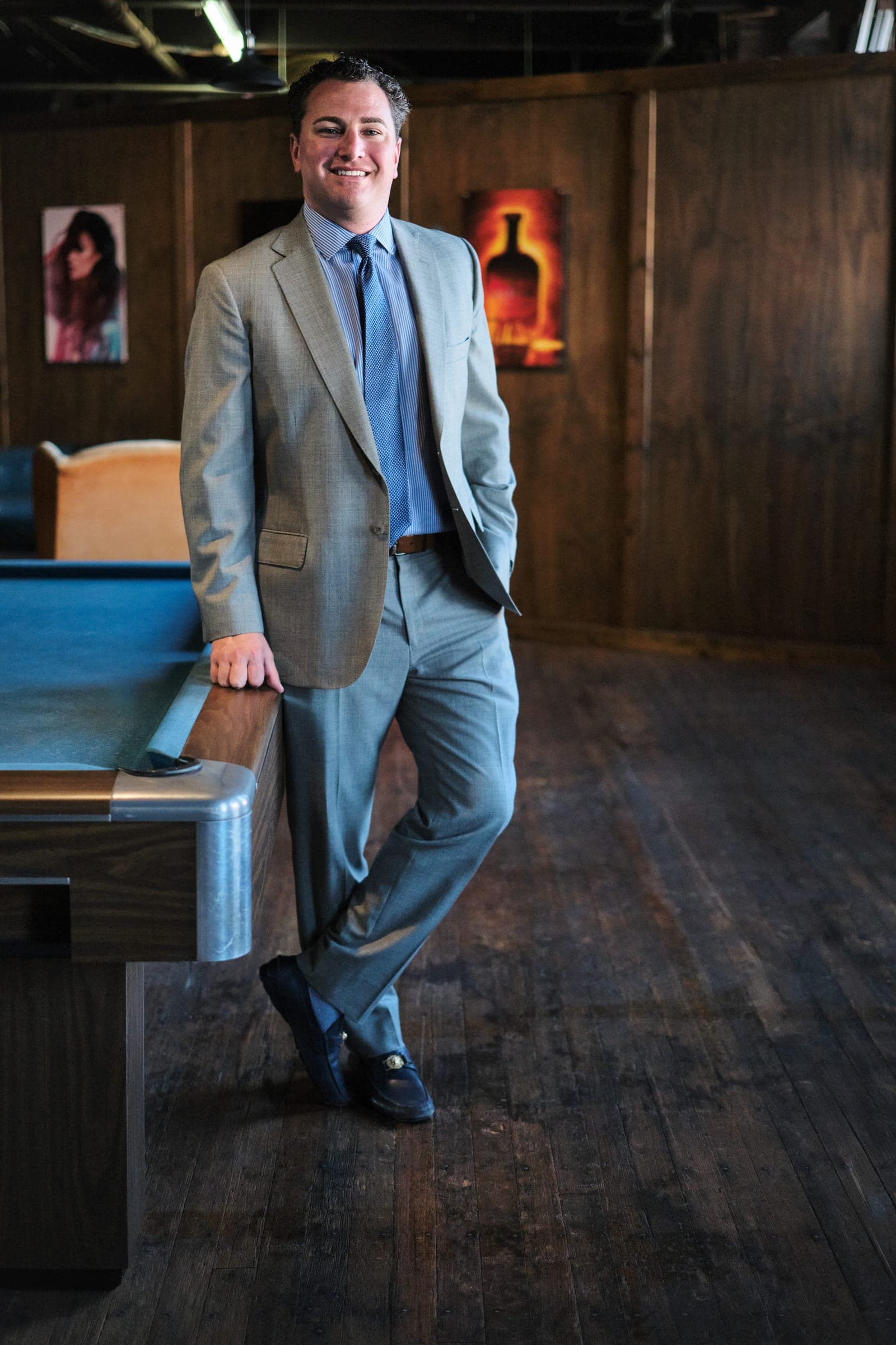Attorney at The Dixon Injury Firm in a light gray suit leaning on a pool table in a wood-panelled room, environmental portrait in St. Louis by Henry David Photography