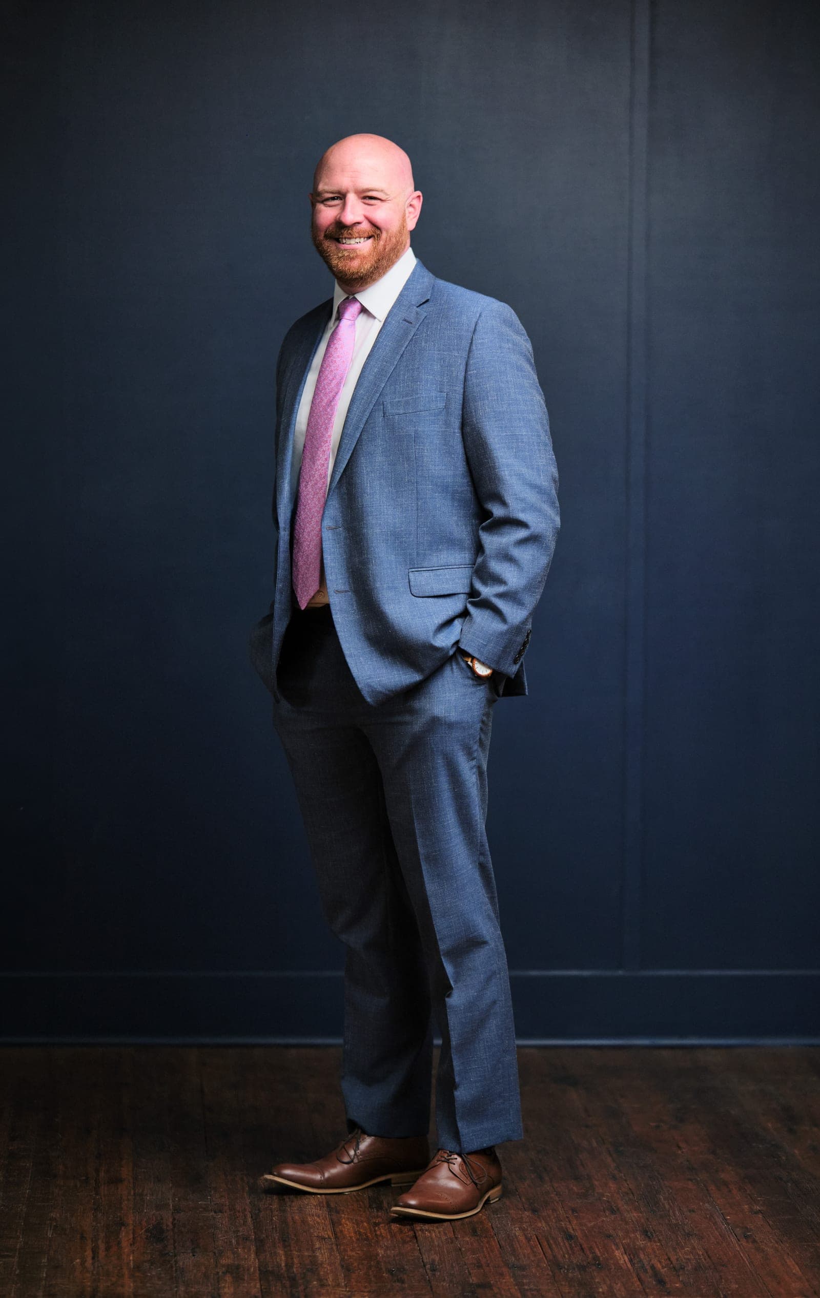 Full-length portrait of an attorney at The Dixon Injury Firm in a light blue suit and pink tie on a navy backdrop over a wood floor in St. Louis by Henry David Photography