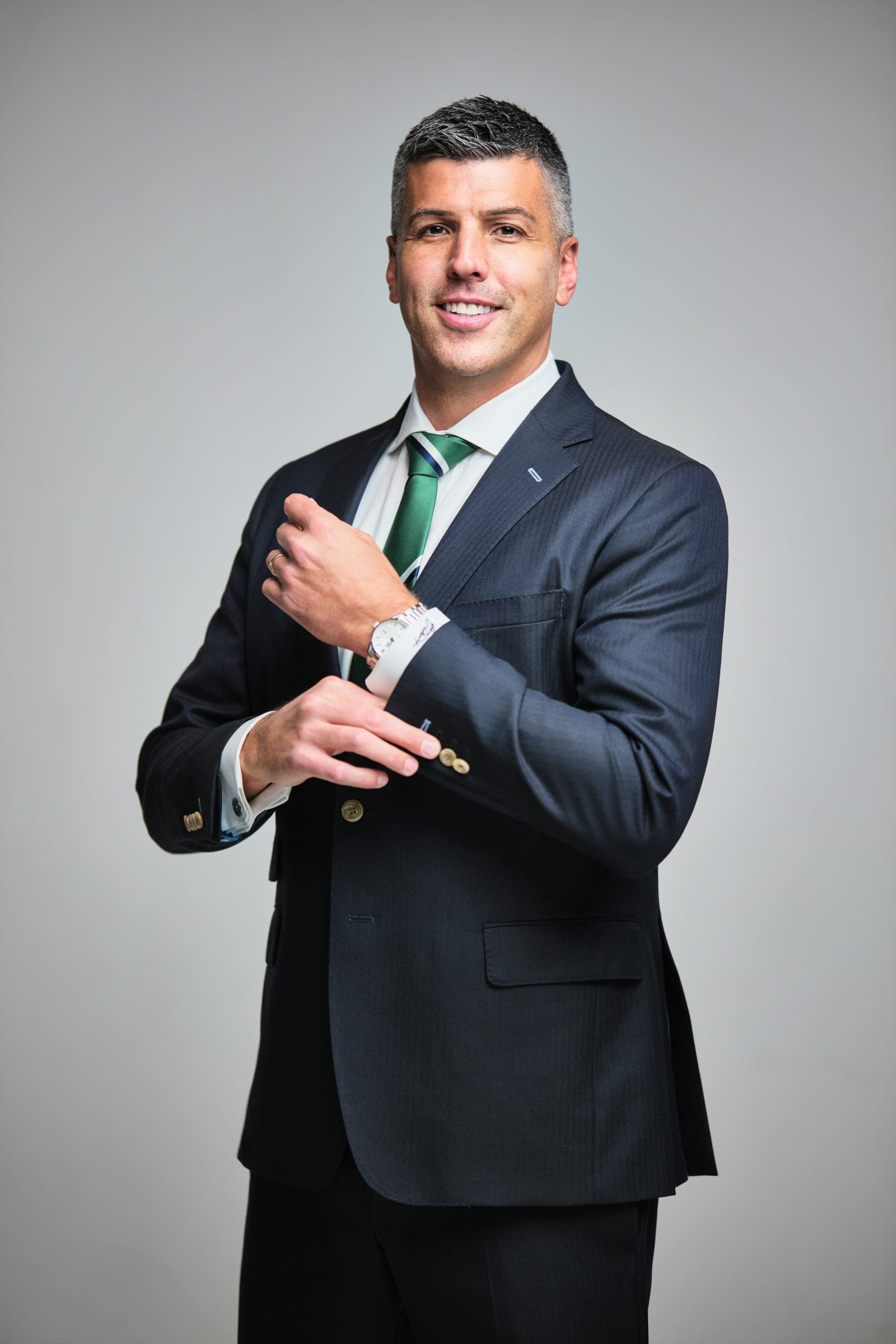 Attorney at The Dixon Injury Firm adjusting a shirt cuff, dark suit and green striped tie on a light gray backdrop, St. Louis law firm portrait by Henry David Photography