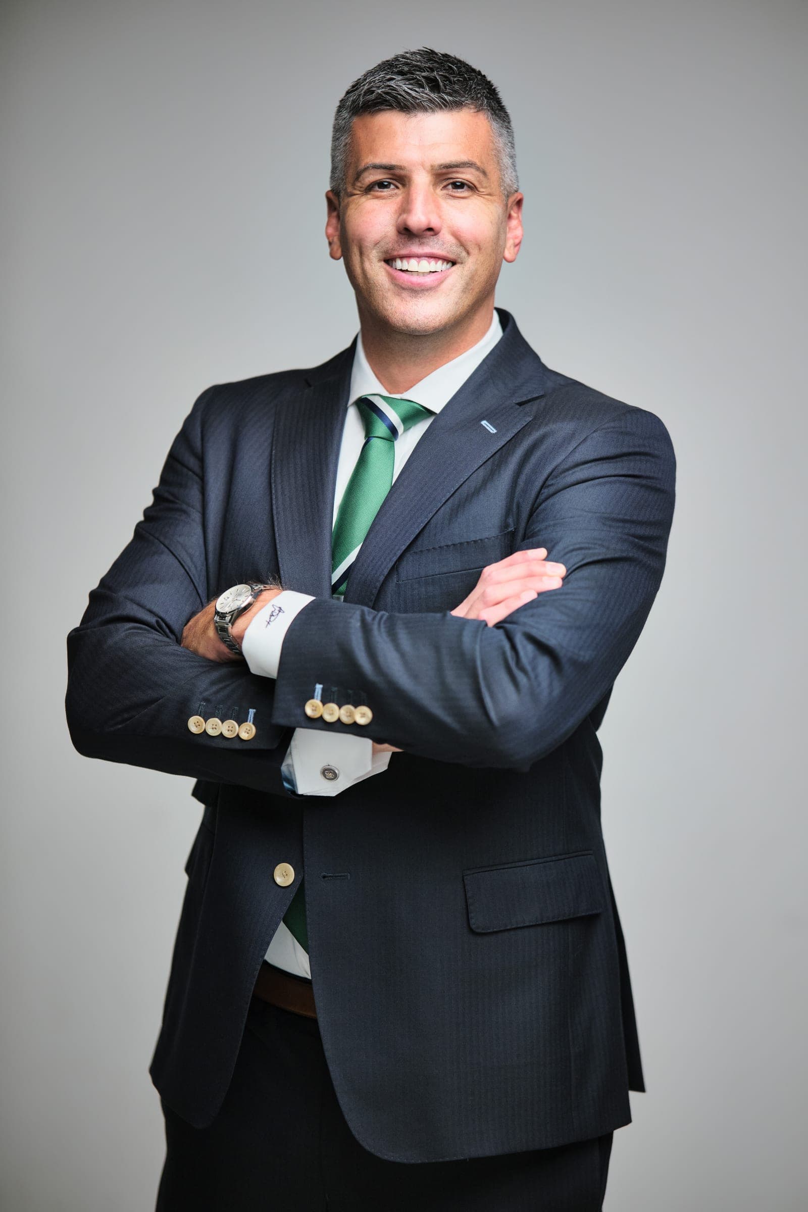 Attorney at The Dixon Injury Firm with arms crossed in a dark suit and green striped tie, smiling, on a light gray backdrop in St. Louis by Henry David Photography