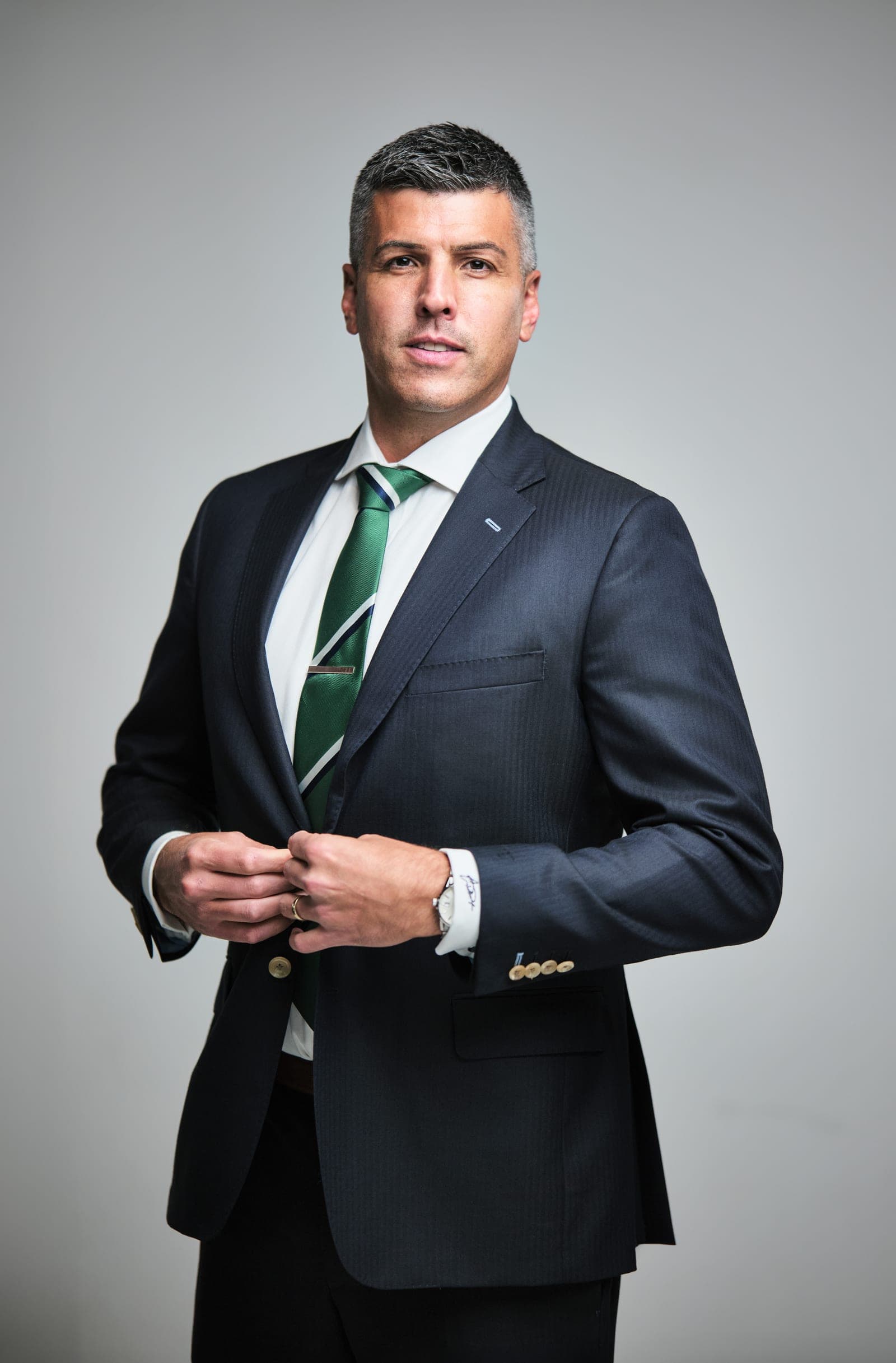 Attorney at The Dixon Injury Firm in a dark suit and green striped tie, buttoning his jacket, portrait on a light gray backdrop in St. Louis by Henry David Photography