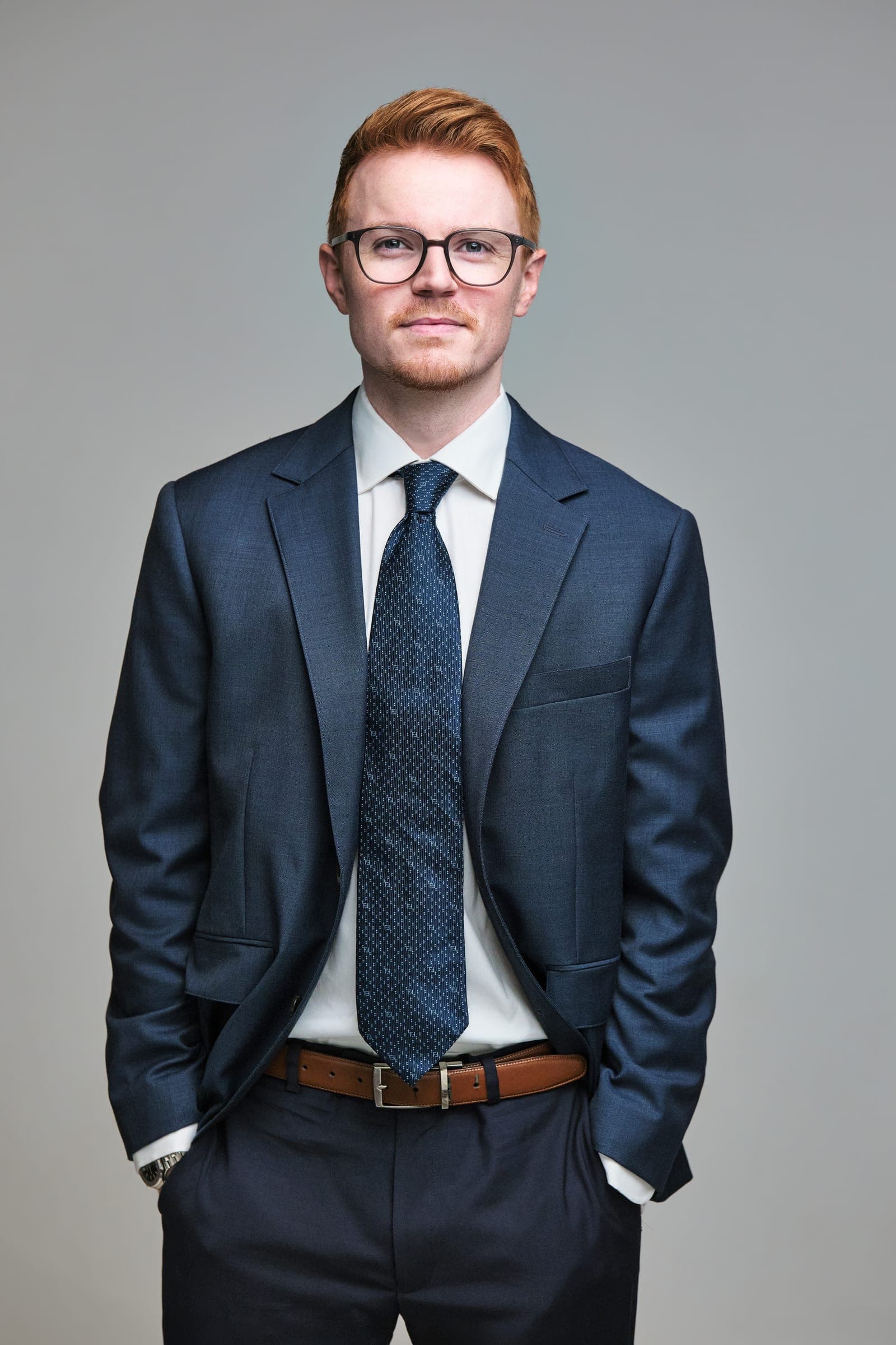 Attorney at The Dixon Injury Firm in a navy suit and patterned tie with hands in pockets, portrait on a light gray backdrop in St. Louis by Henry David Photography