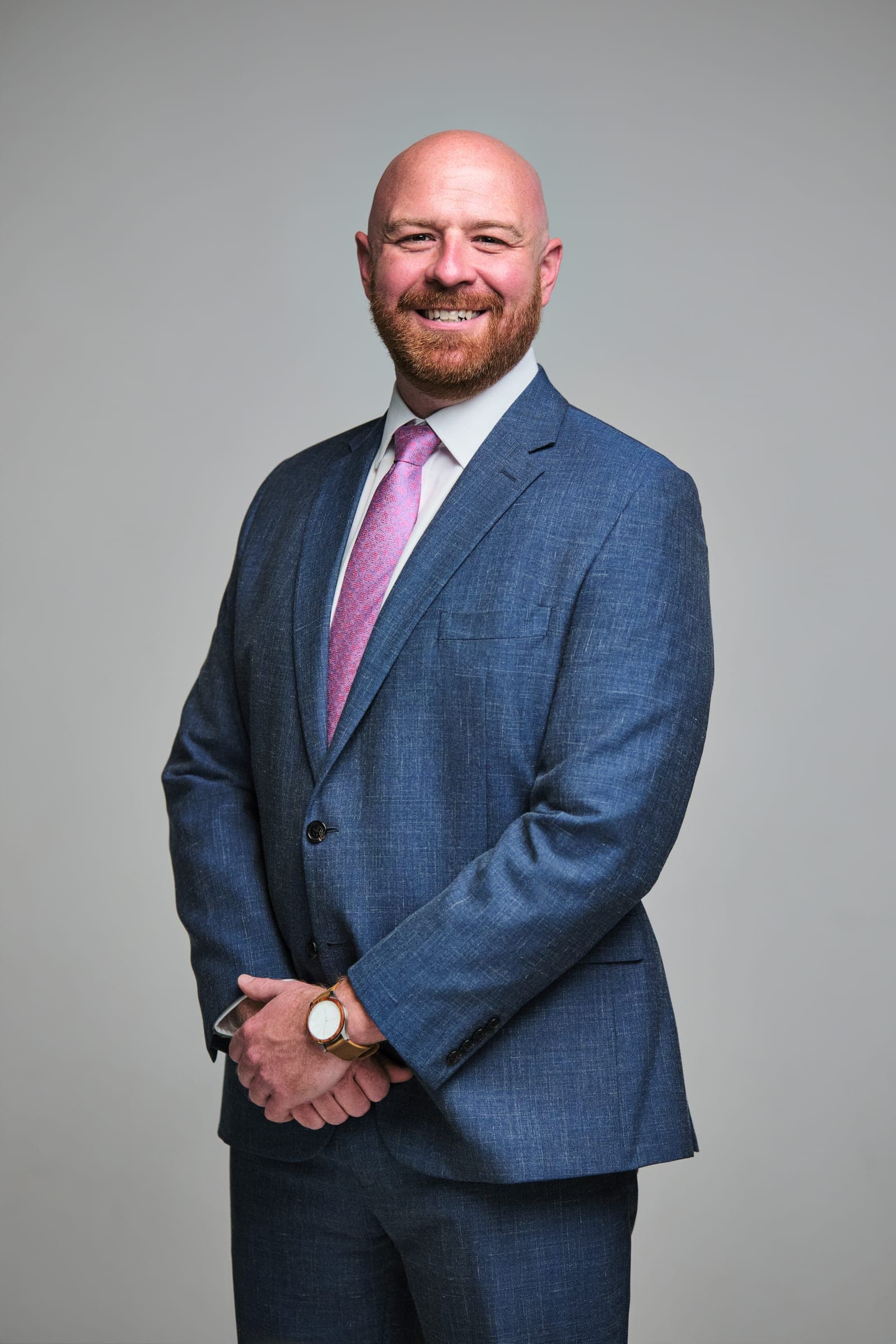 Attorney at The Dixon Injury Firm in a light blue suit and pink tie, hands clasped, portrait on a light gray backdrop in St. Louis by Henry David Photography