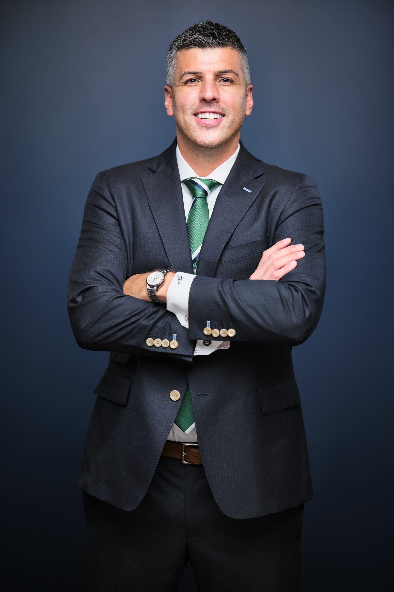 Attorney at The Dixon Injury Firm in a dark suit and green striped tie, arms crossed, three-quarter portrait on a navy backdrop in St. Louis by Henry David Photography