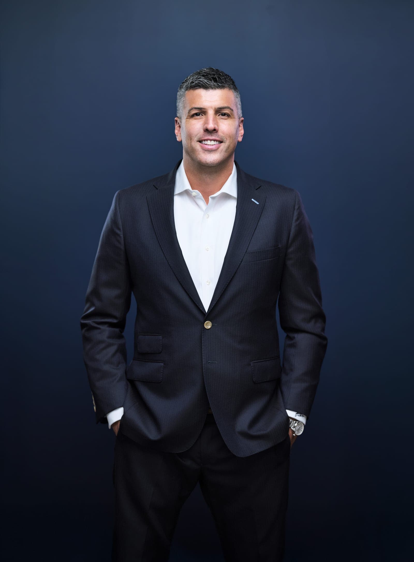 Attorney at The Dixon Injury Firm in a dark suit and open-collar white shirt, hands in pockets, portrait on a navy backdrop in St. Louis by Henry David Photography