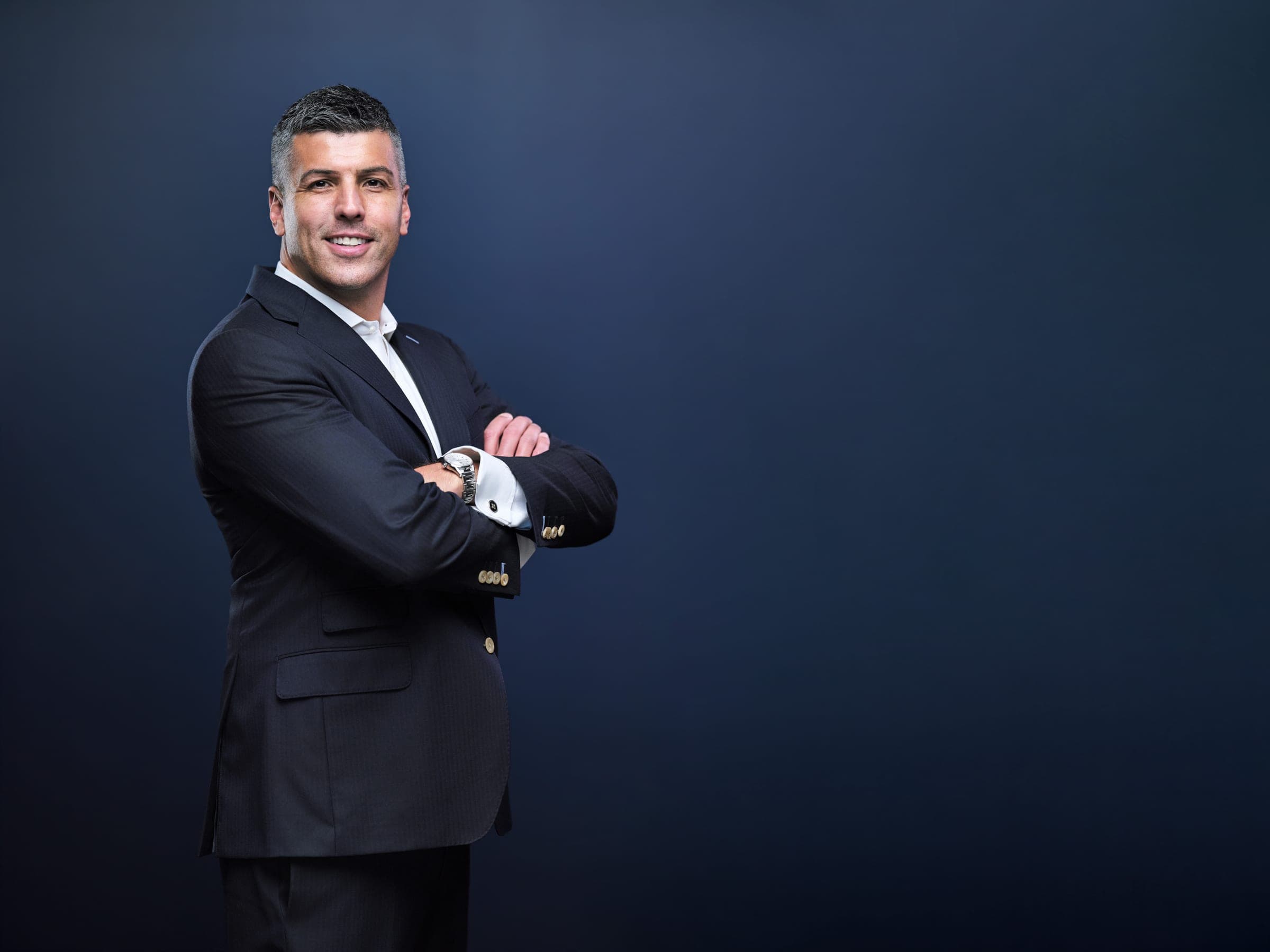 Attorney at The Dixon Injury Firm turned to the side with arms crossed, dark suit and open collar, wide portrait with open navy backdrop for text, St. Louis by Henry David Photography