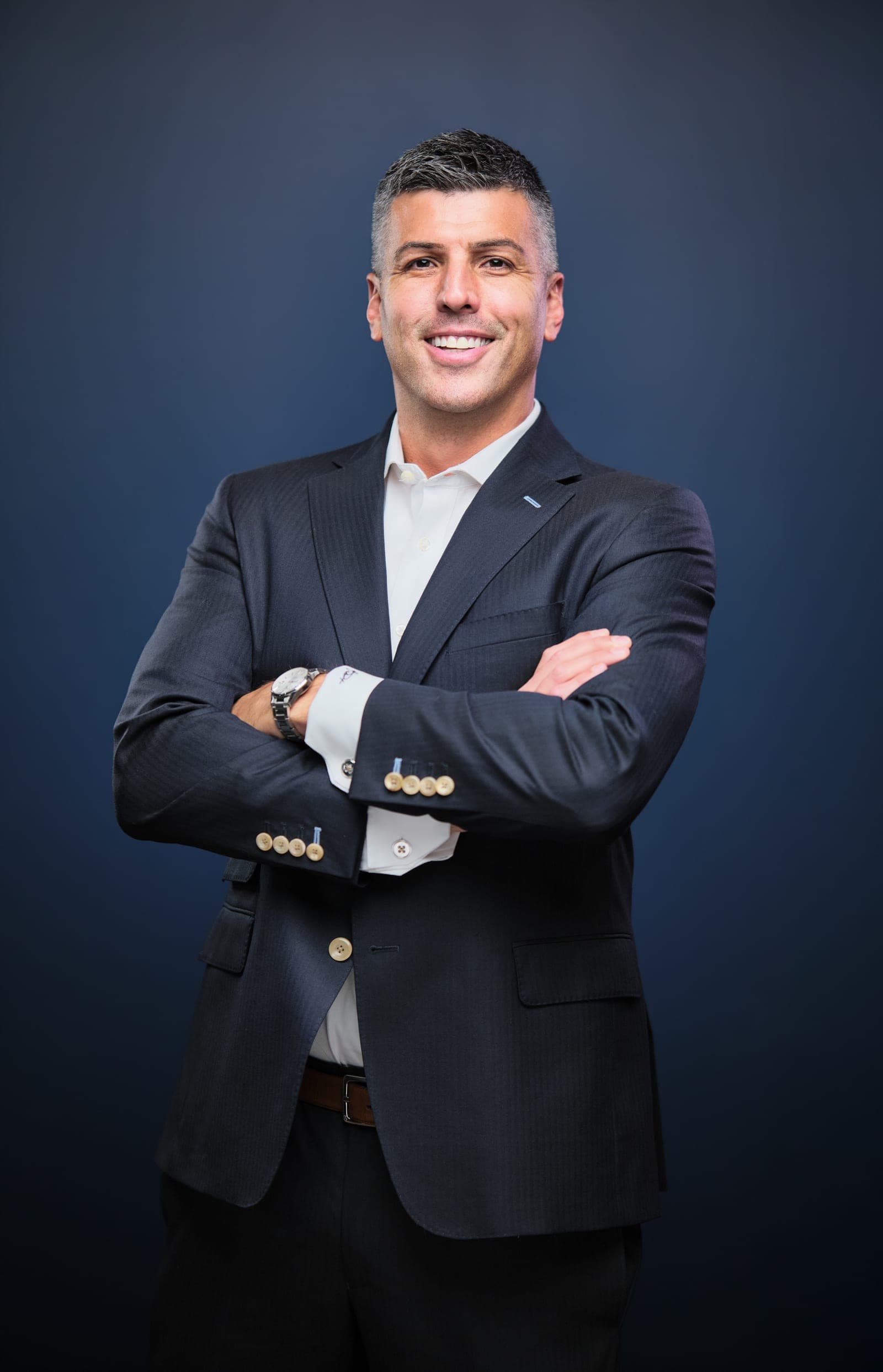 Attorney at The Dixon Injury Firm in a dark suit and open-collar white shirt, arms crossed, portrait on a navy backdrop in St. Louis by Henry David Photography