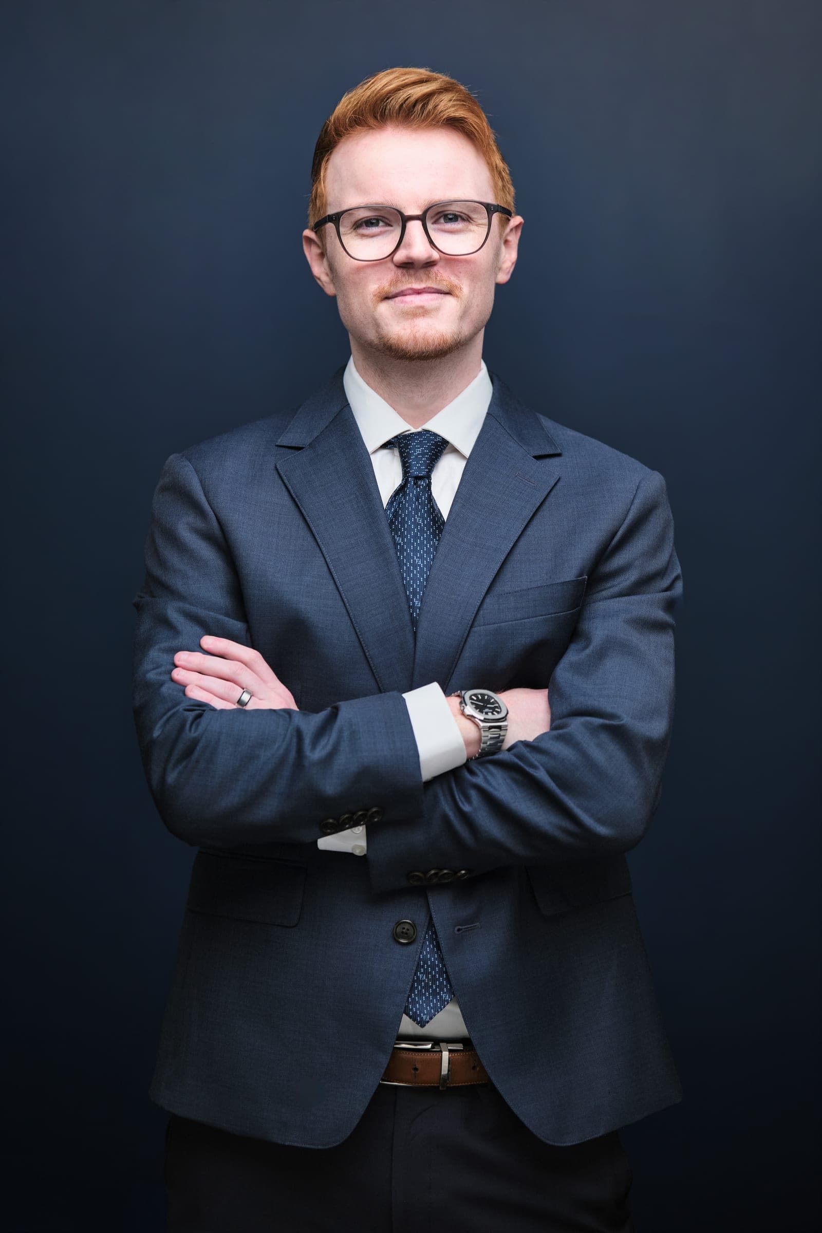 Attorney at The Dixon Injury Firm in a navy suit, patterned tie and glasses, arms crossed, portrait on a navy backdrop in St. Louis by Henry David Photography