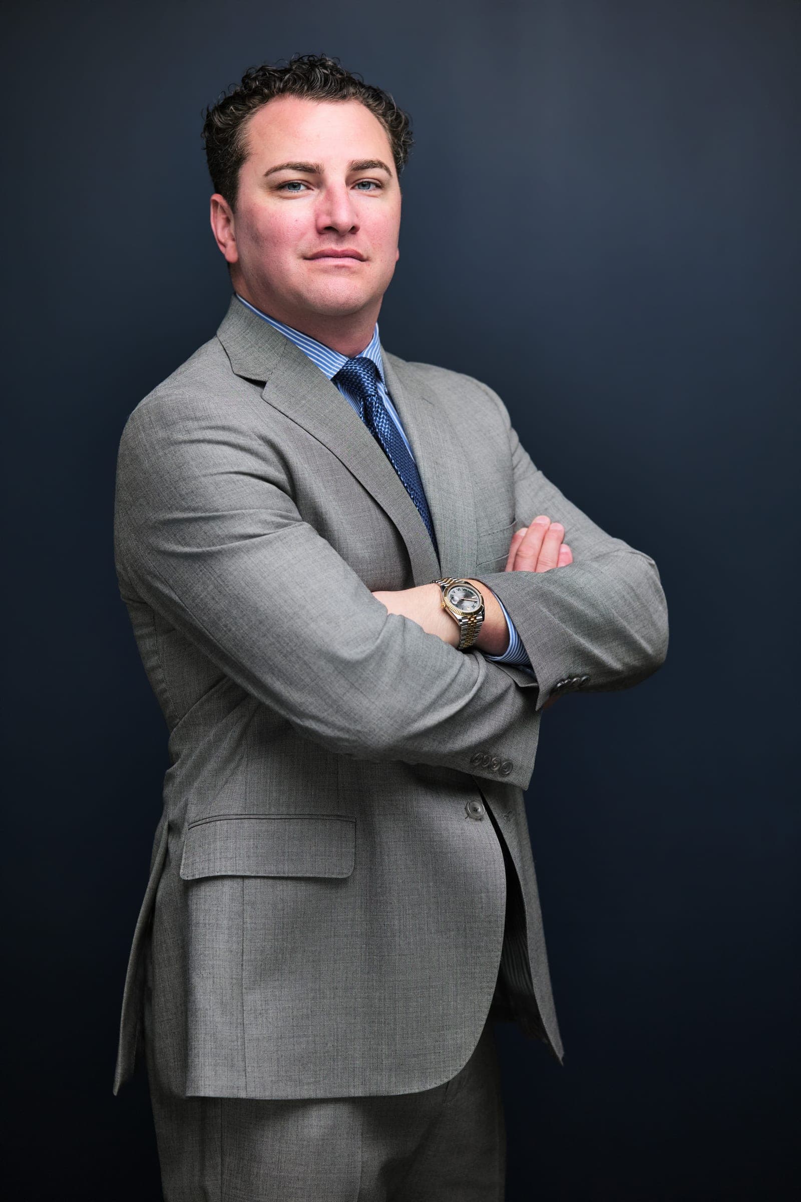Attorney at The Dixon Injury Firm in a light gray suit, blue shirt and navy tie, arms crossed, portrait on a navy backdrop in St. Louis by Henry David Photography
