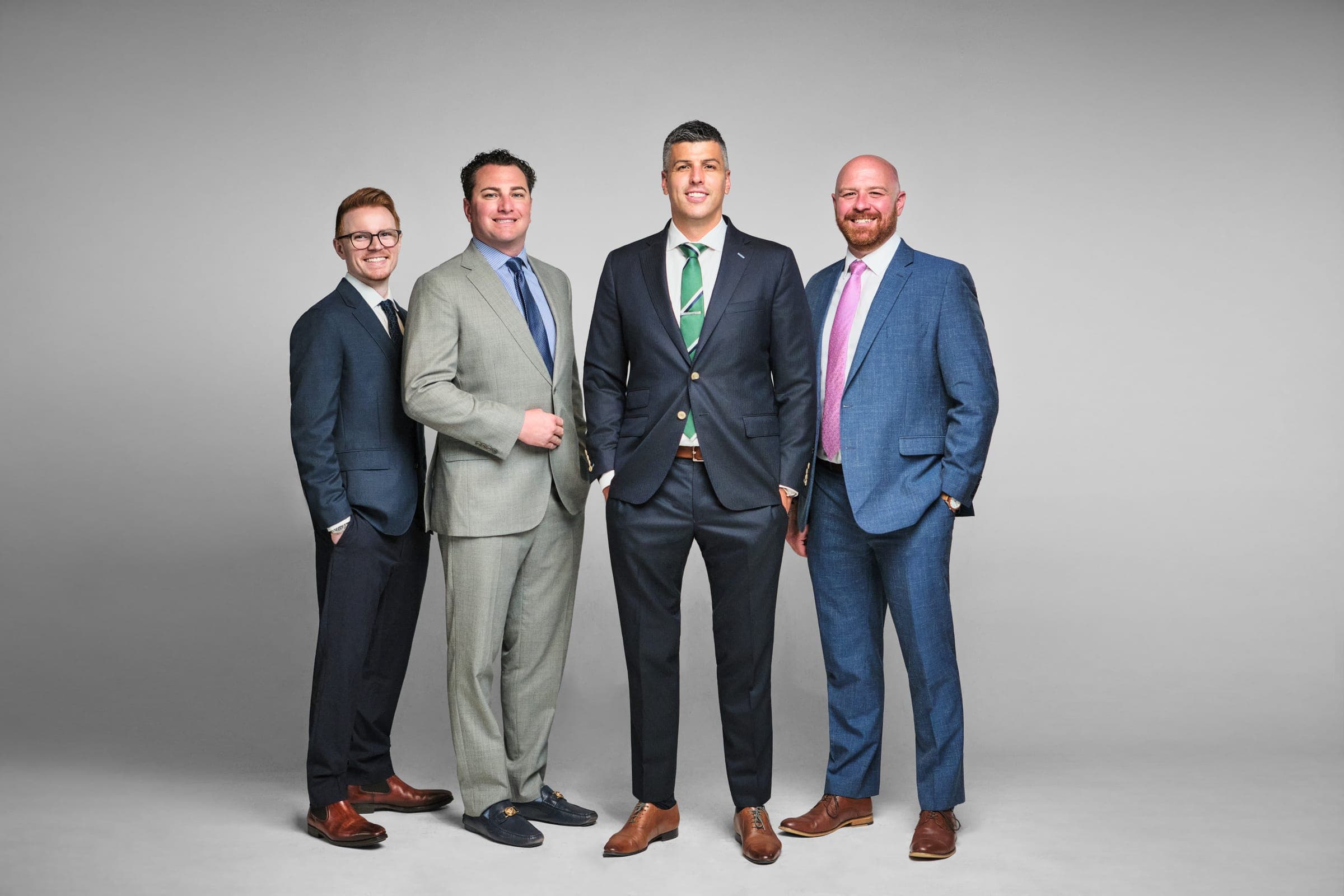 All four attorneys of The Dixon Injury Firm, a St. Louis personal injury law firm, standing together on a light gray backdrop, team photo by Henry David Photography