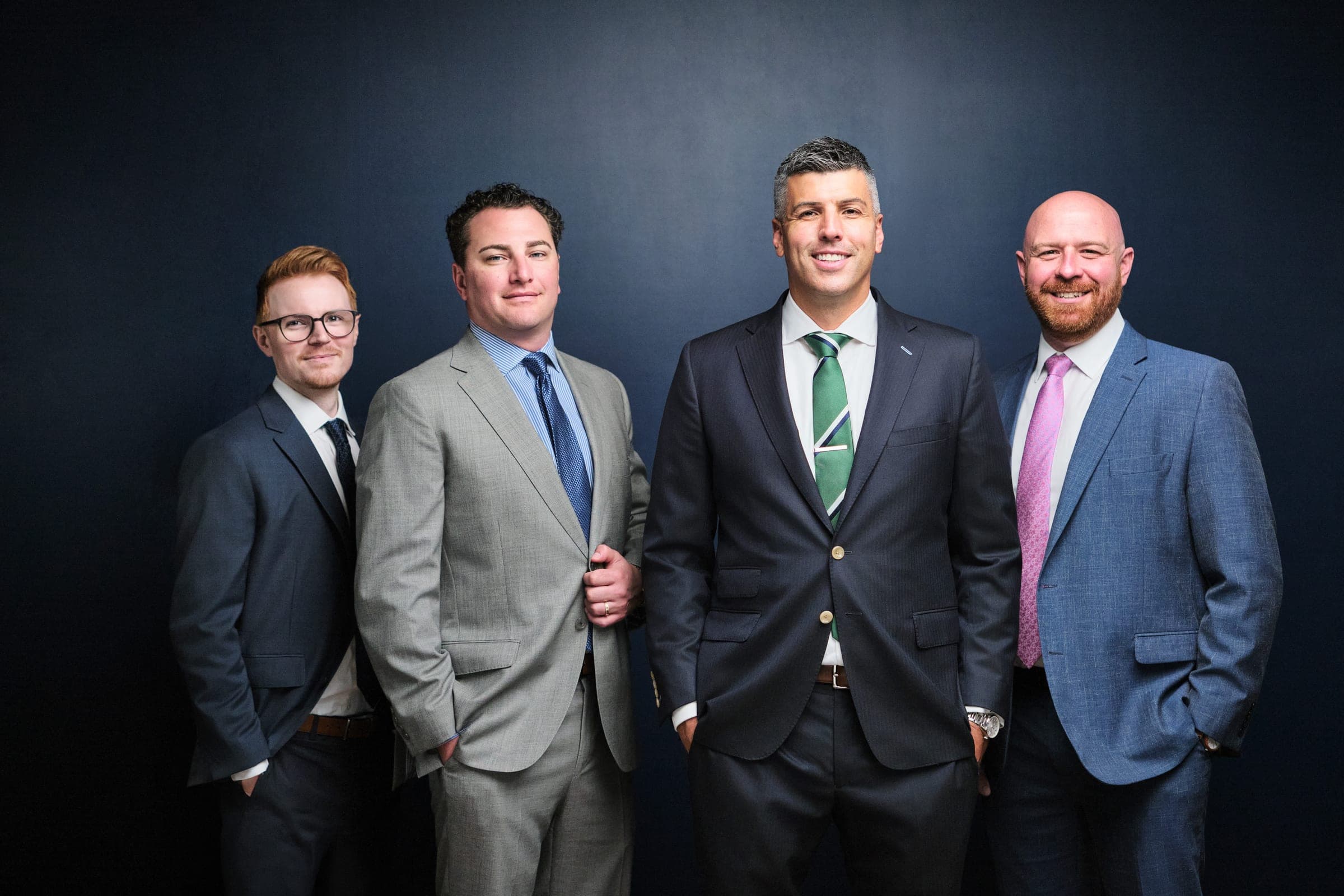 The four attorneys of The Dixon Injury Firm standing shoulder to shoulder on a navy backdrop, St. Louis law firm team photo by Henry David Photography