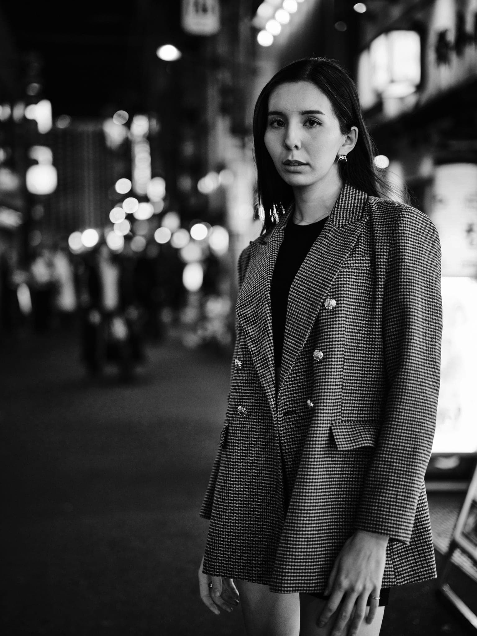 Emilia photographed in a houndstooth blazer on a Tokyo street at night