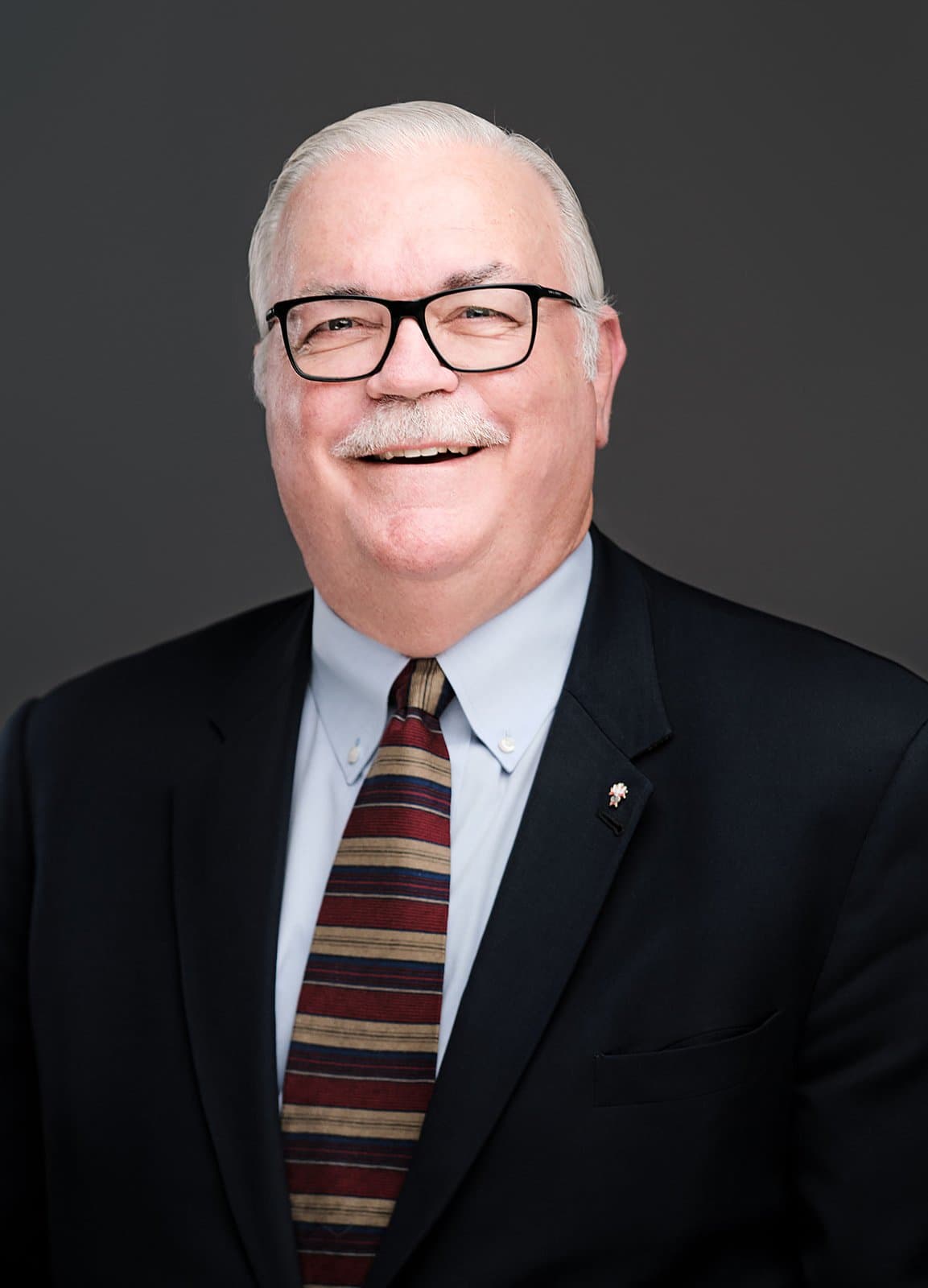 Older man in a dark suit and patterned tie, photographed at a conference headshot booth