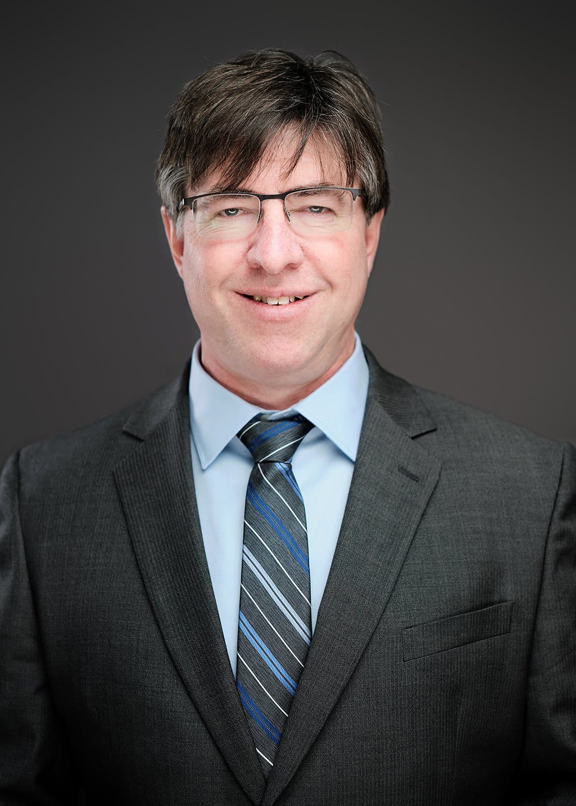 Bearded man in glasses, a checked shirt and grey jacket, photographed at a conference headshot booth