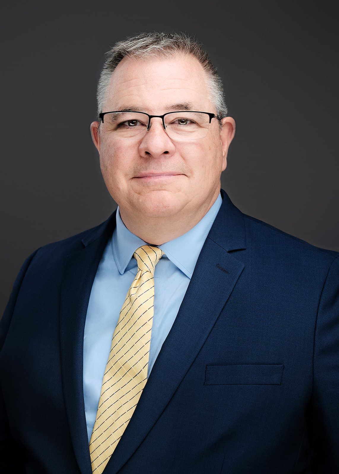 Man in a dark suit and light shirt, photographed at a conference headshot booth