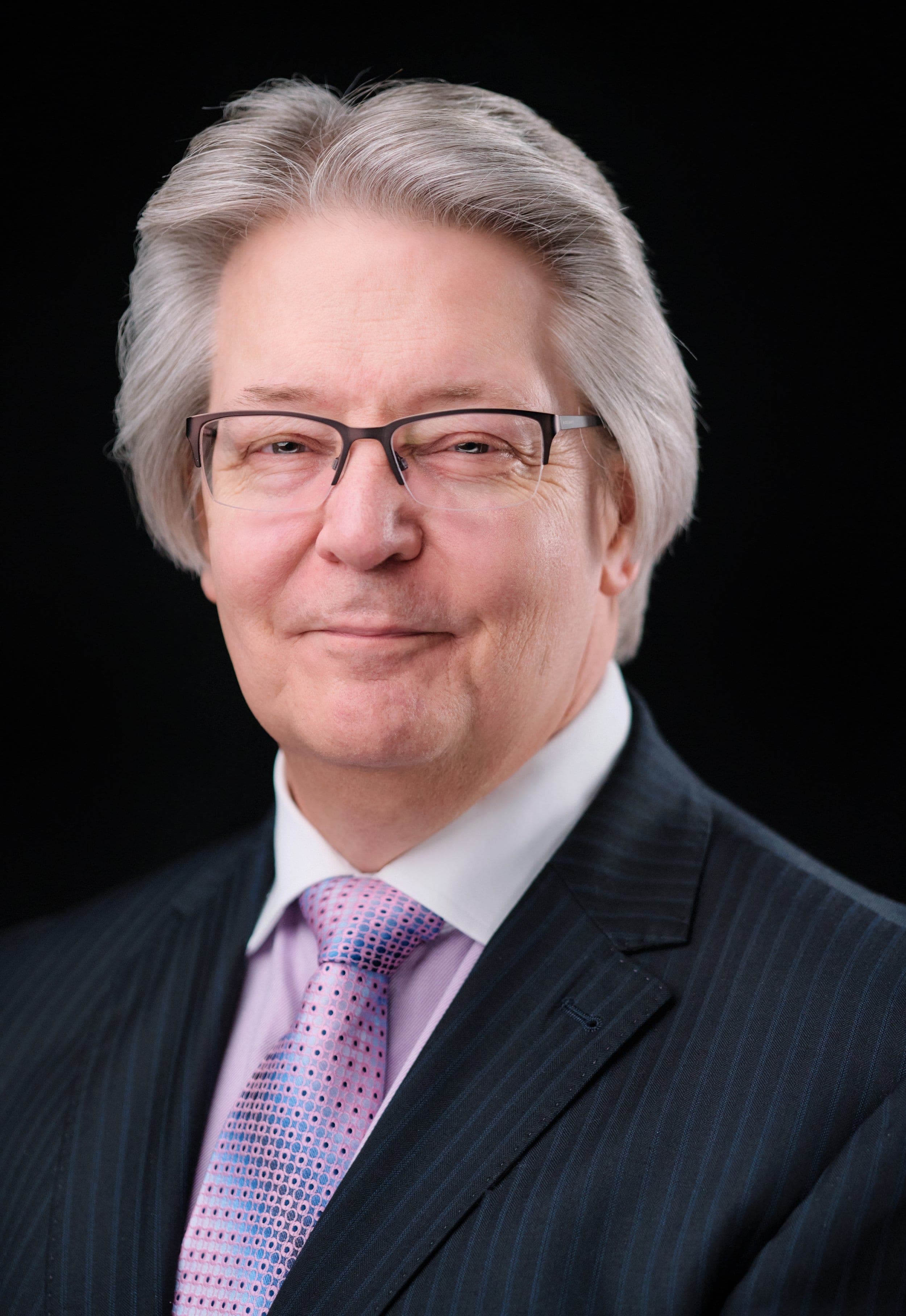 Man with silver hair and glasses in a pinstripe suit and lavender tie, photographed at our headshot booth at a business expo