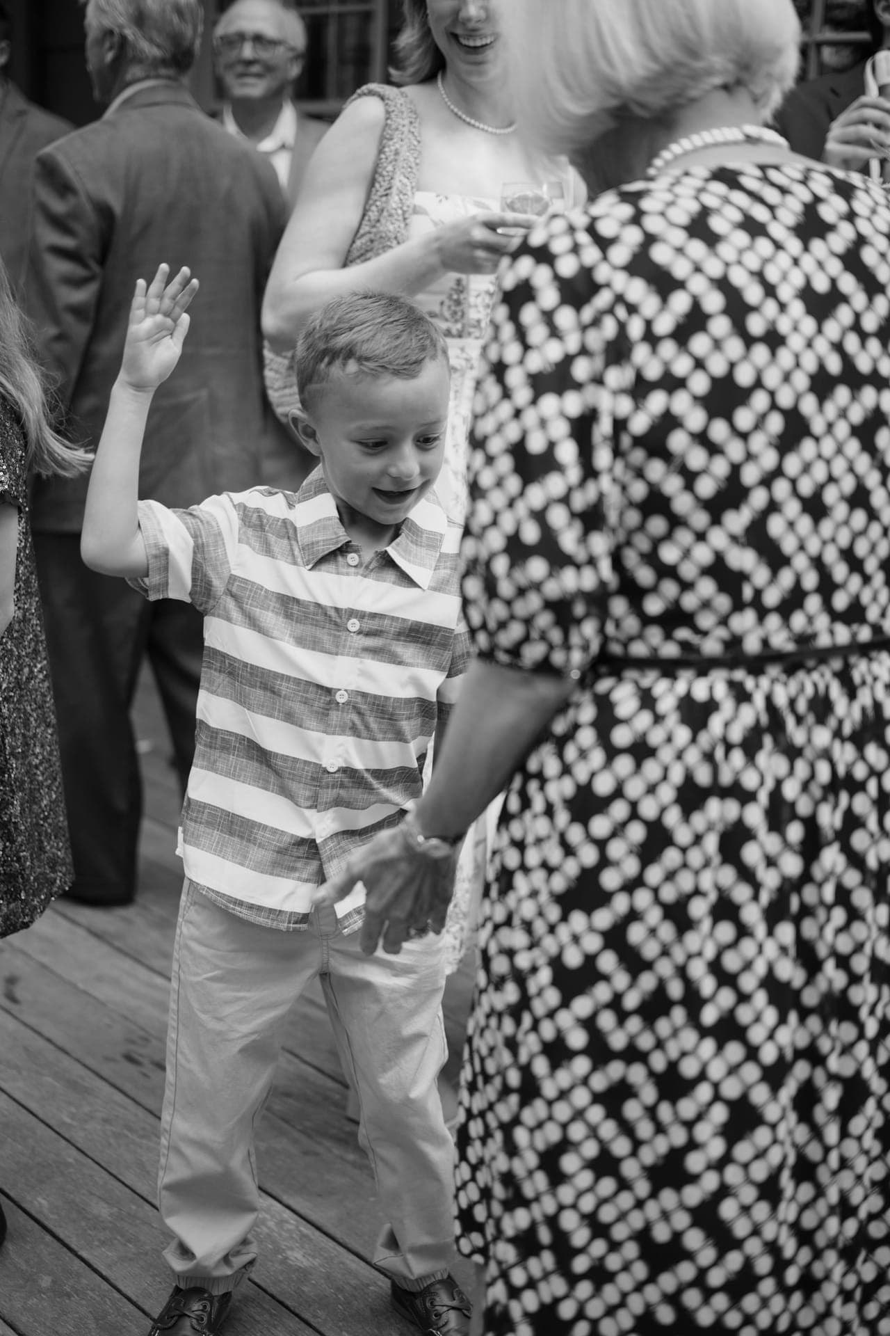 Black and white photo of a young boy waving with a grin at a family reunion in Ladue