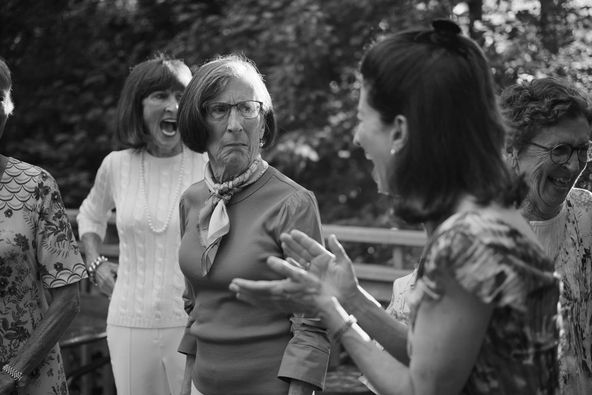 Black and white candid of a woman laughing behind a deadpan child at a family reunion in Ladue