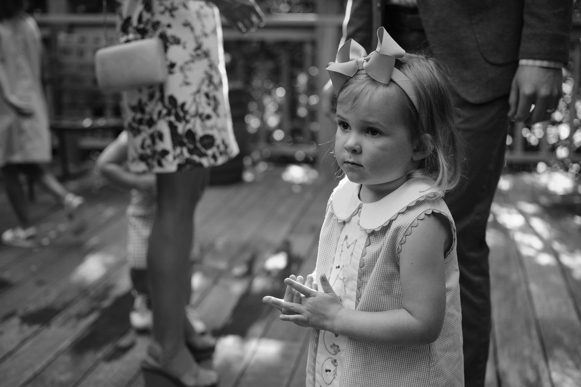 Black and white photo of a young girl in a bow watching the party among the adults at a family reunion in Ladue