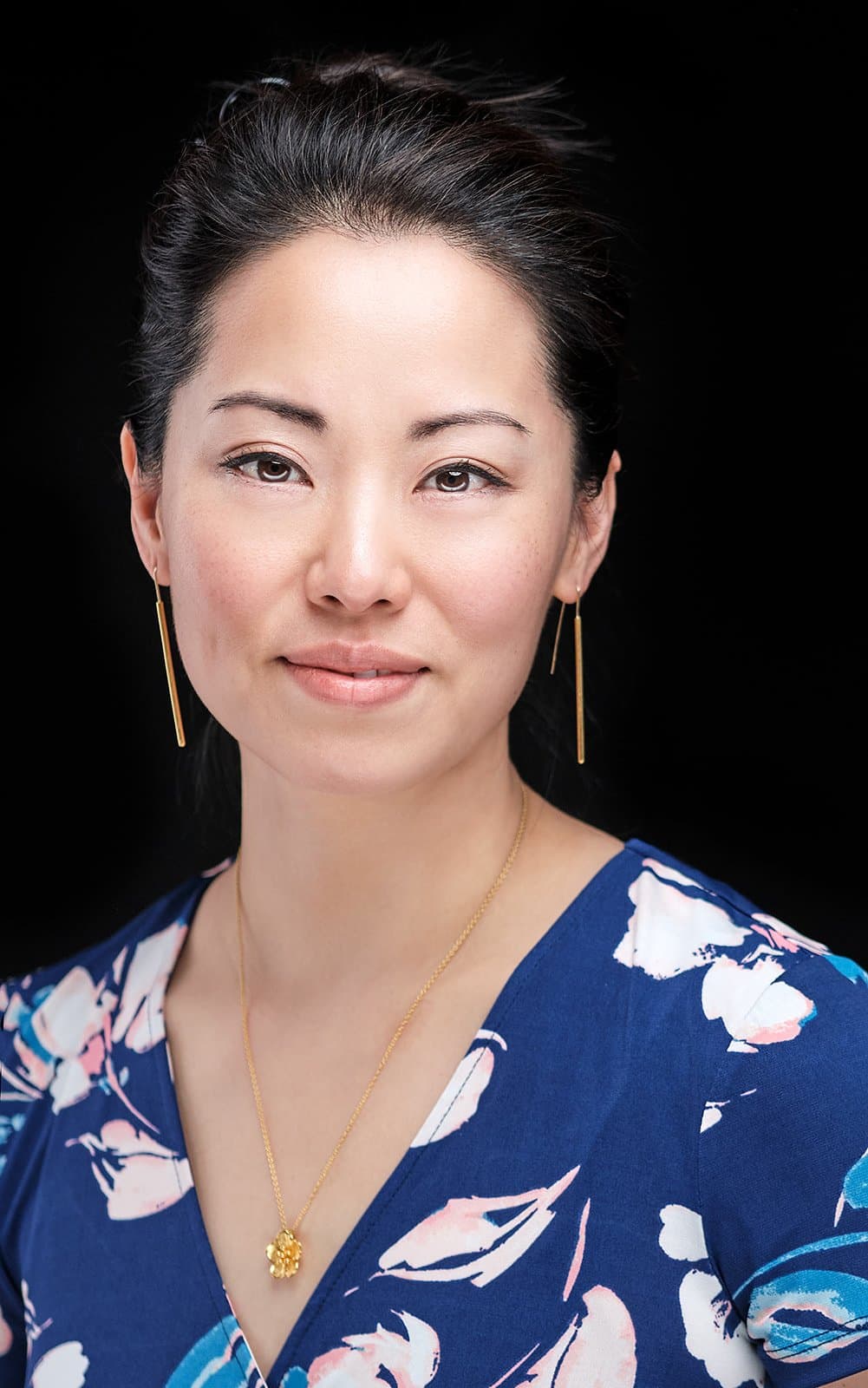 Woman with dark hair pulled back in a blue floral dress, photographed at our headshot booth at a new media expo