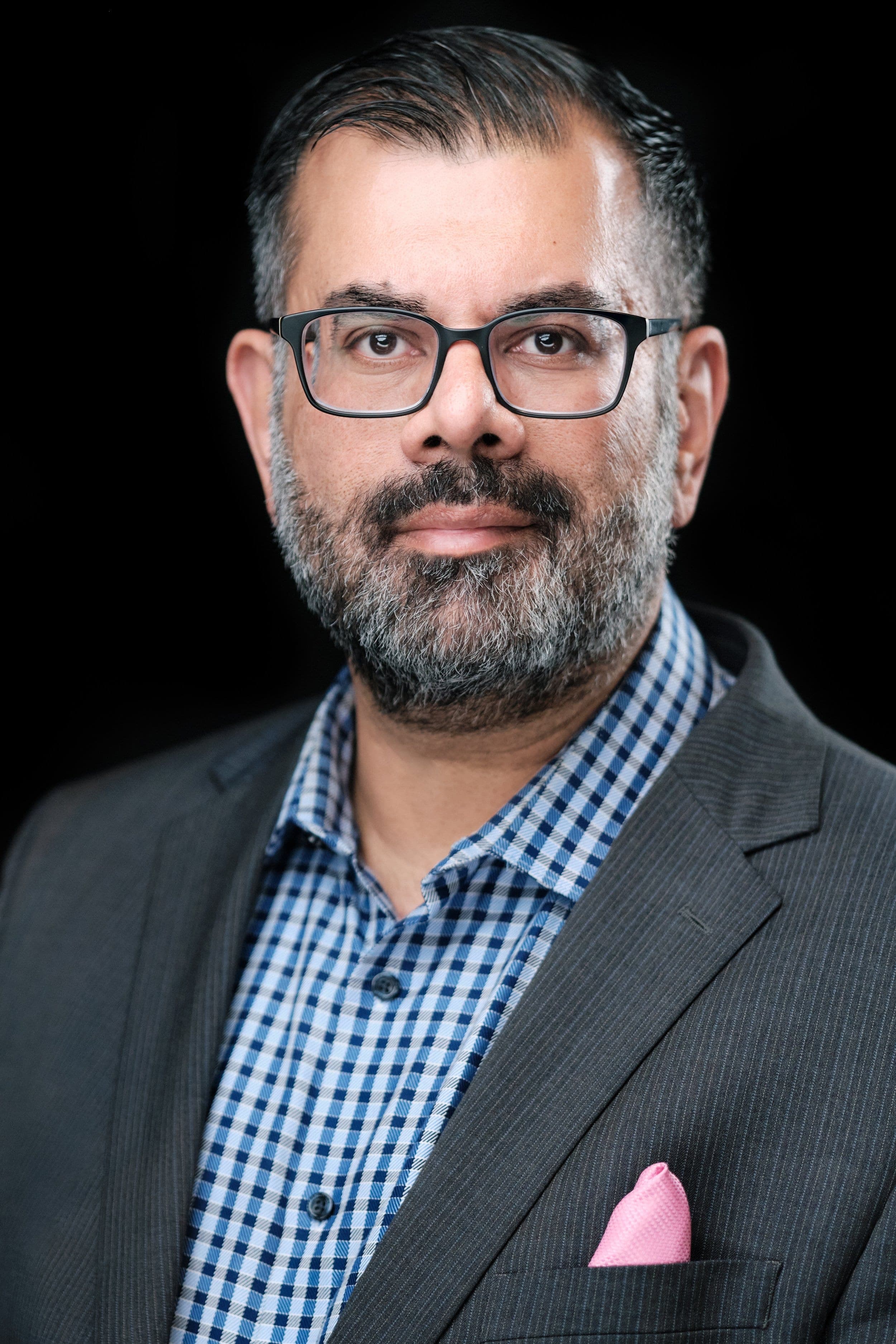 Man in glasses with a close beard and grey suit, photographed at a conference headshot booth