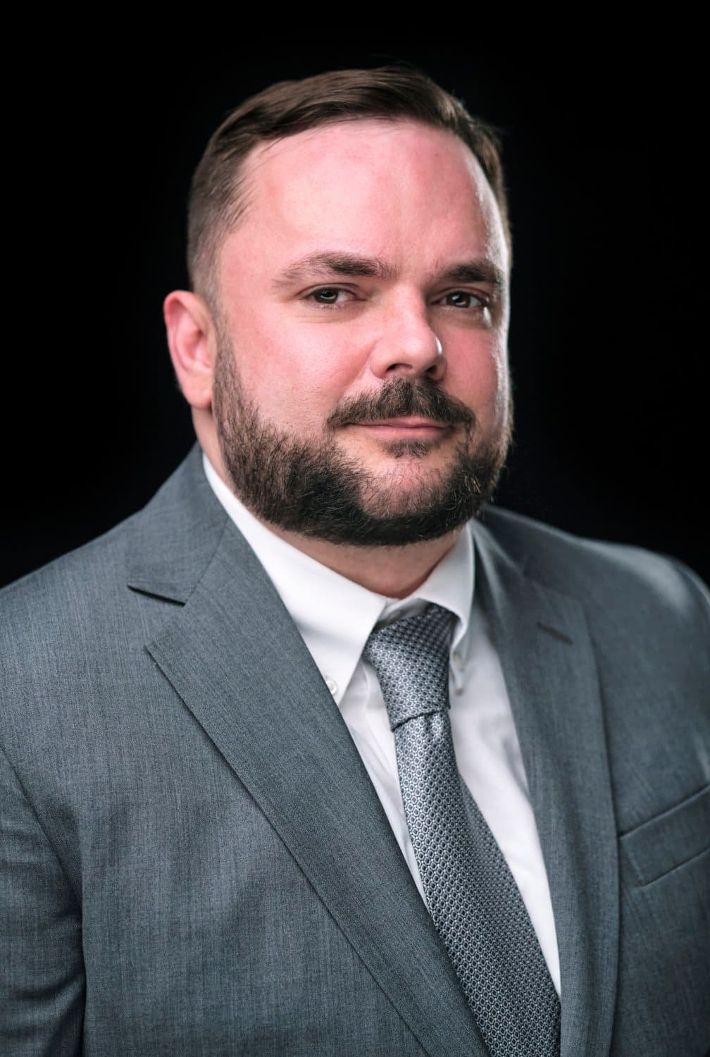 Bearded man in a dark suit and pale tie, photographed at a conference headshot booth