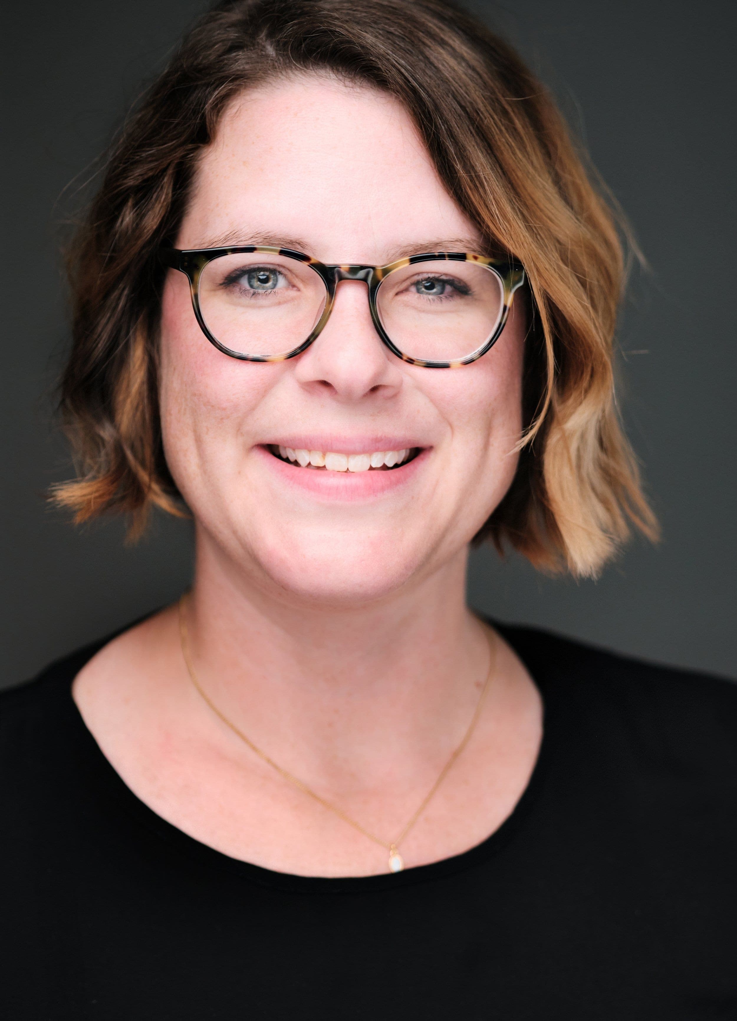 Woman in round glasses with a dark bob, photographed at a conference headshot booth