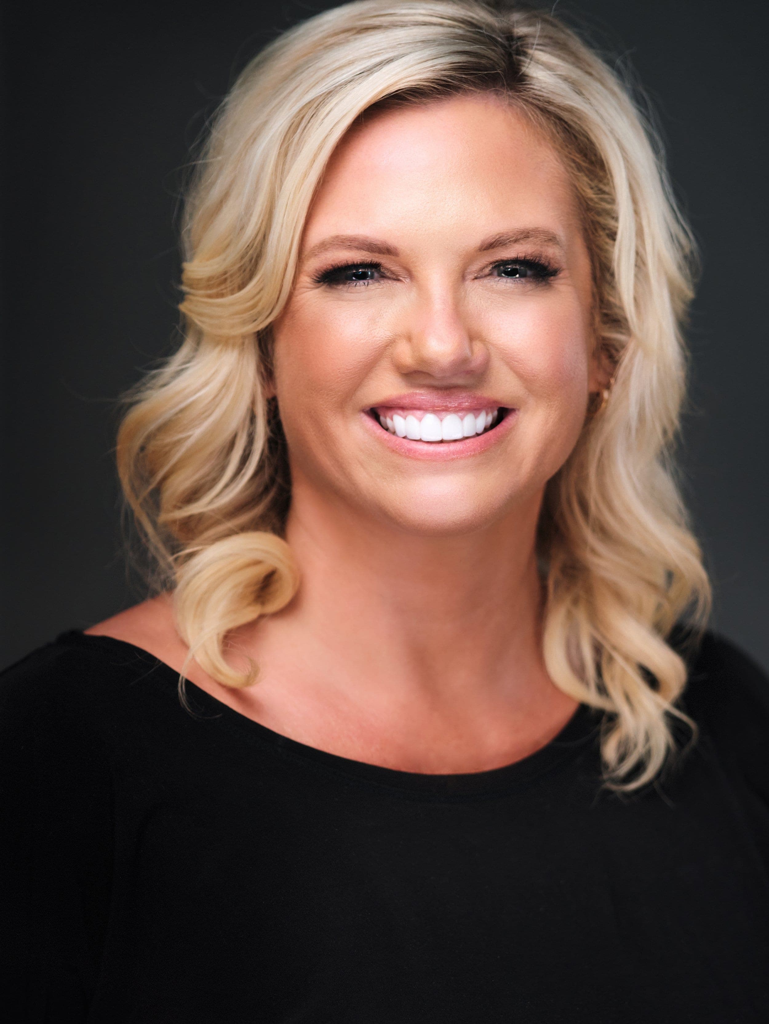 Woman with long blonde hair in a black top, photographed at a conference headshot booth
