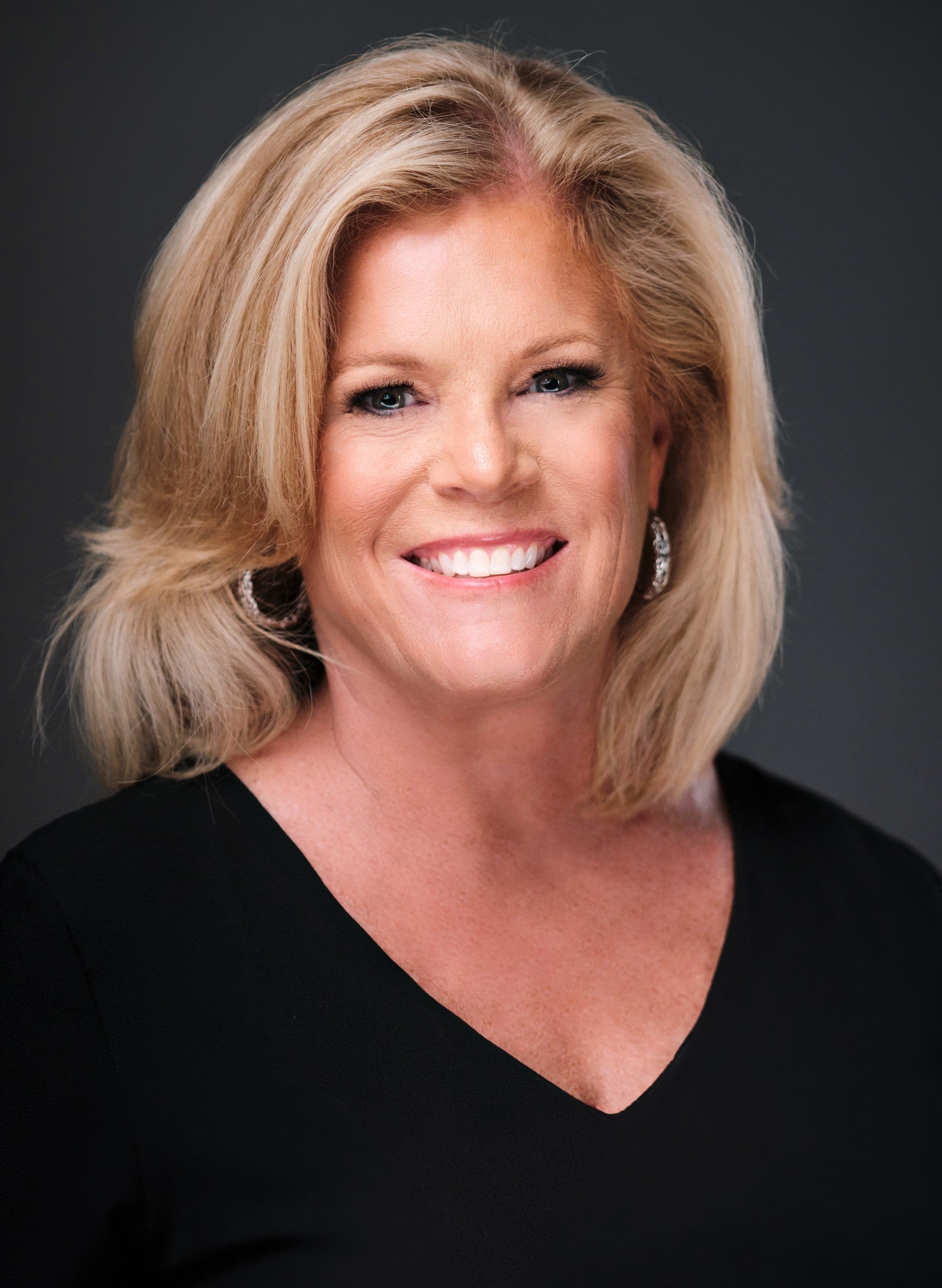 Woman with long blonde hair in a black top, photographed at a conference headshot booth