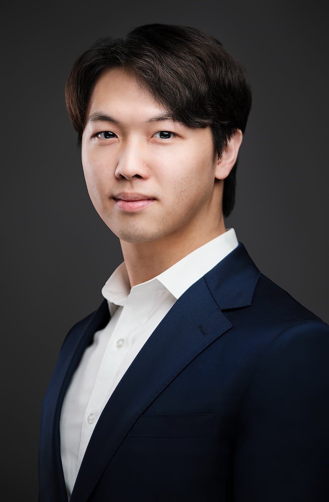 Man with dark hair in a dark suit and white shirt, photographed at a conference headshot booth