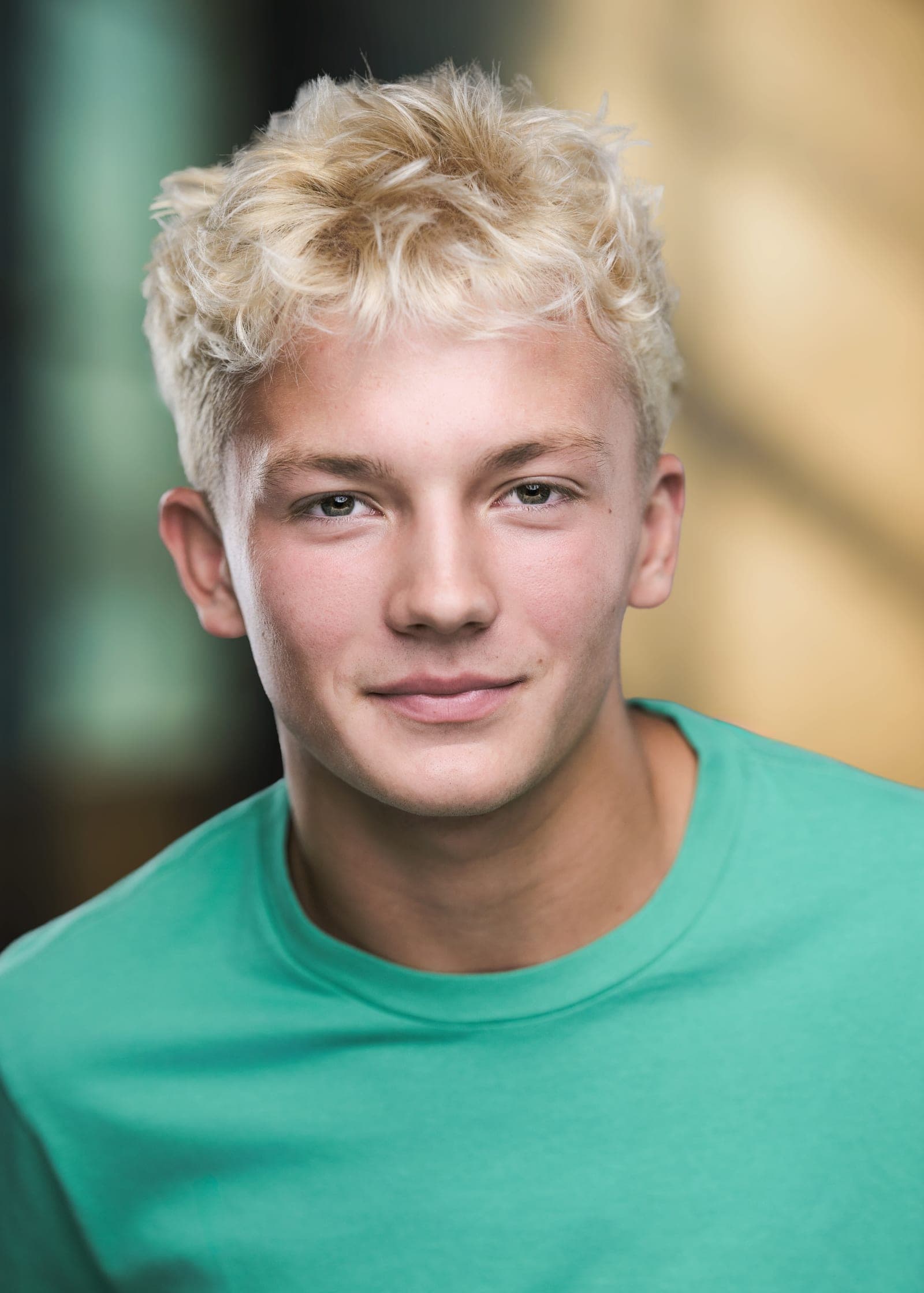 Caden, a young actor in a green crew-neck tee, photographed in soft daylight against a warm out-of-focus background for a commercial acting headshot in St. Louis